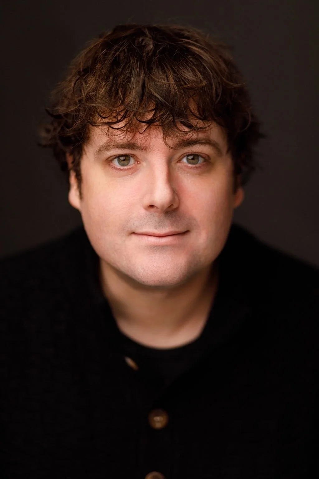 Portrait of Patrick Jordan, Education Director and Co-Founder of EnKore Theatre Company, looking at the camera in a professional headshot against a dark background.