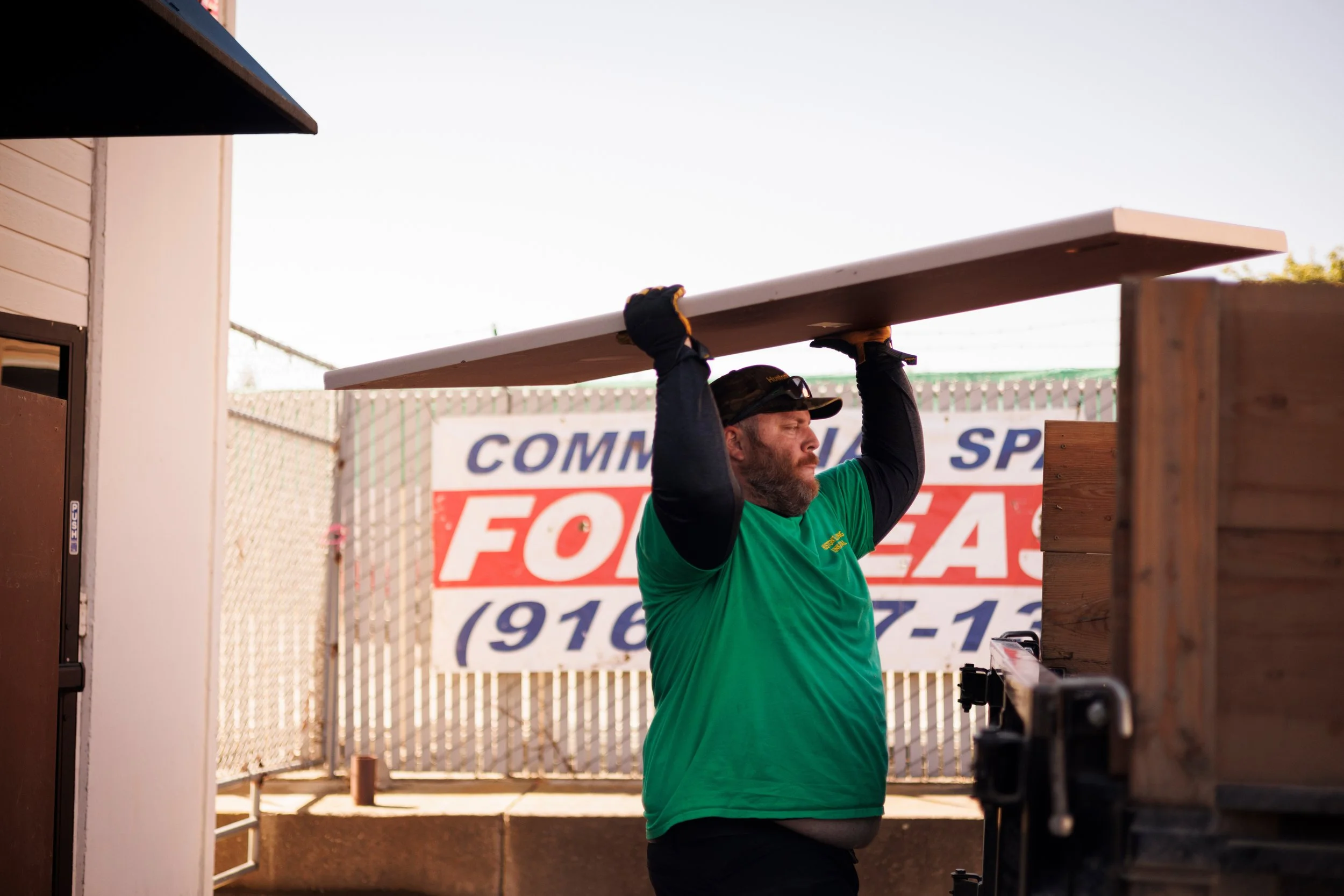 Ross Huston of Huston’s Hauling Junk Removal carrying a dismantled cubicle desk top toward a hauling trailer outside the future EnKore Theatre Company space
