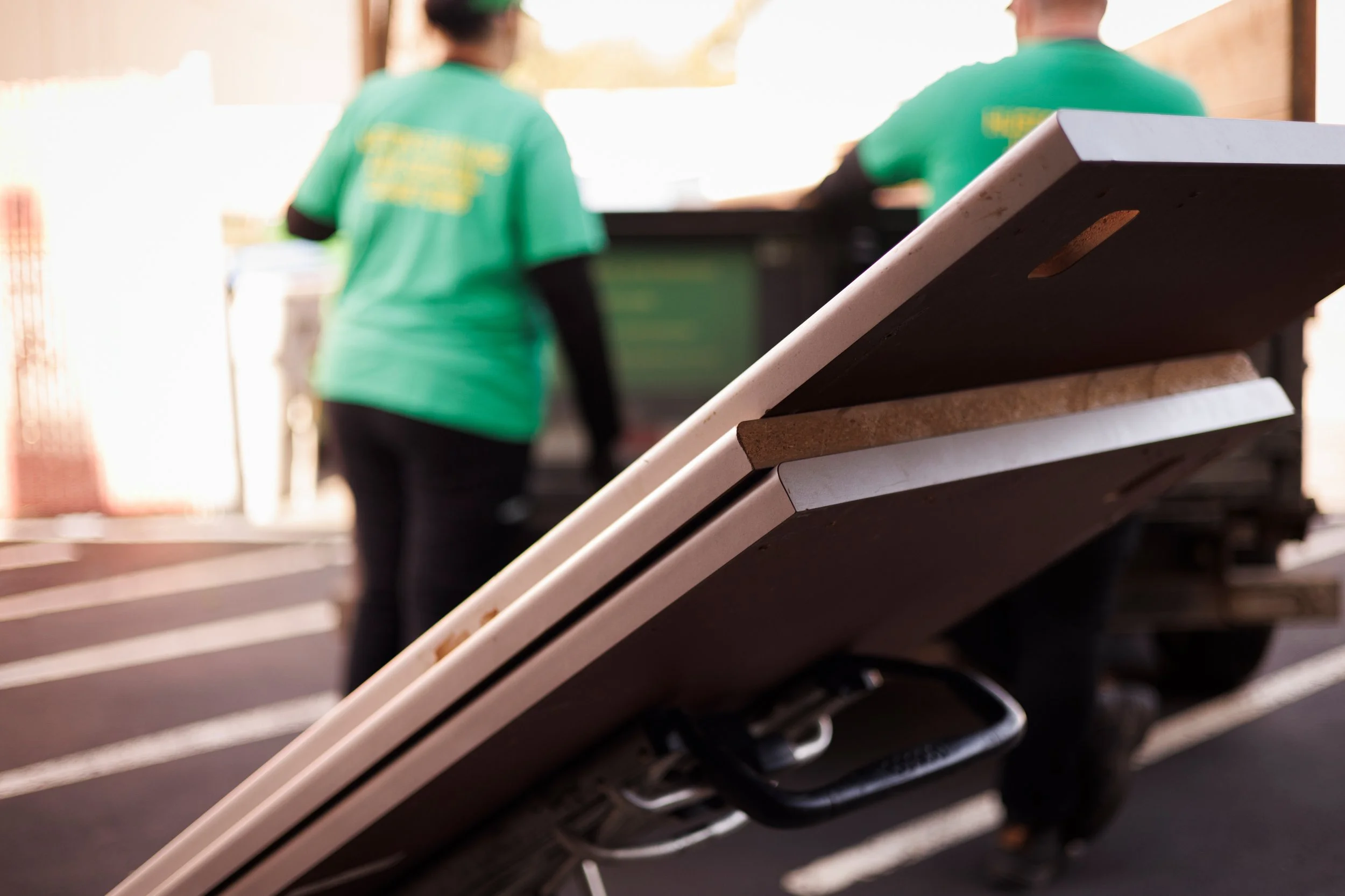 Close-up of dismantled cubicle desk tops stacked on a dolly with members of Huston’s Hauling Junk Removal working in the background outside the future EnKore Theatre Company space.