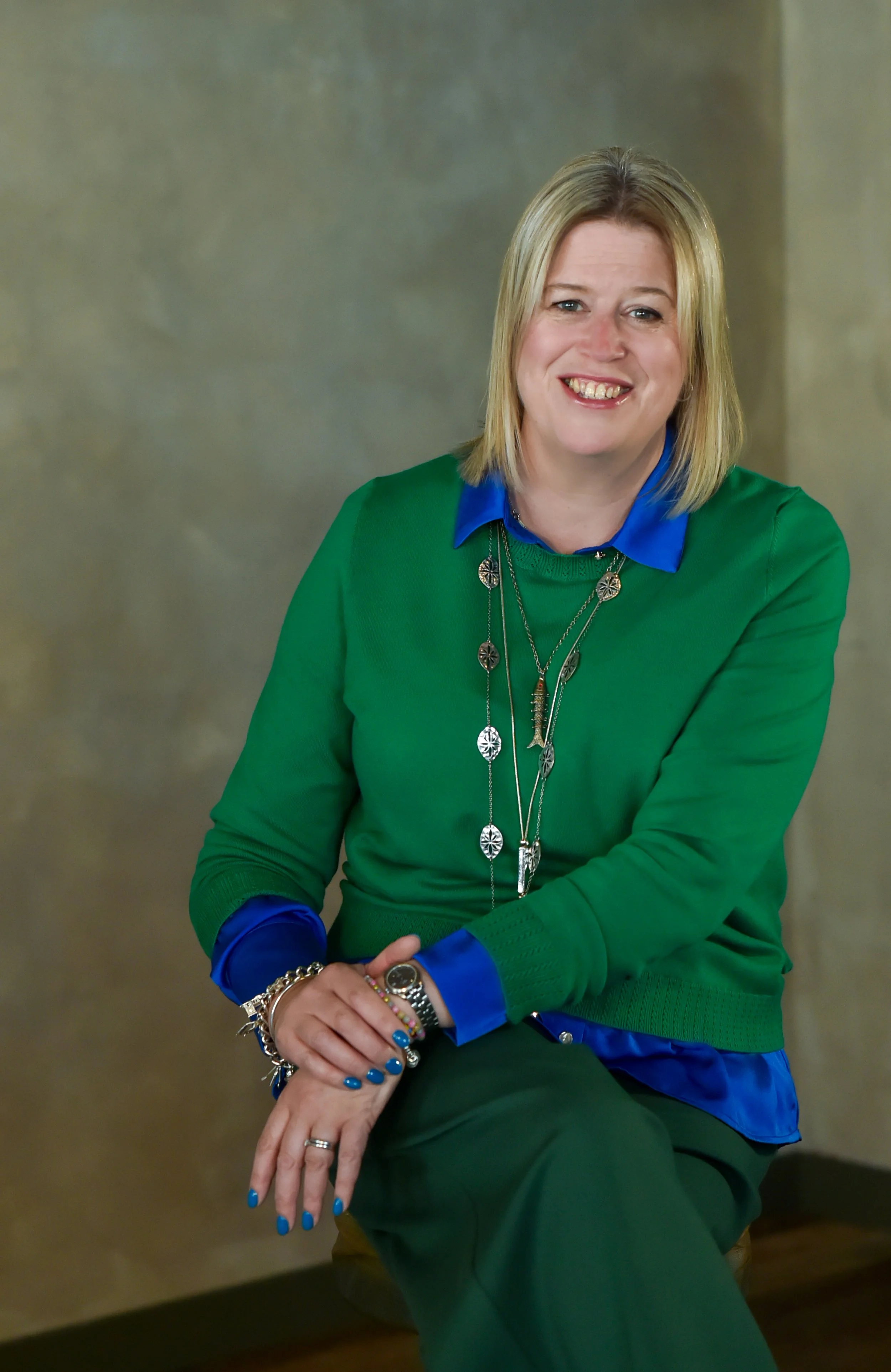 Becky M celebrant for wedding ceremonies and naming ceremonies. Second weddings, adopting family, name changes, renewal of vows. A 50 year old celebrant on a chair. Happy and smiling.