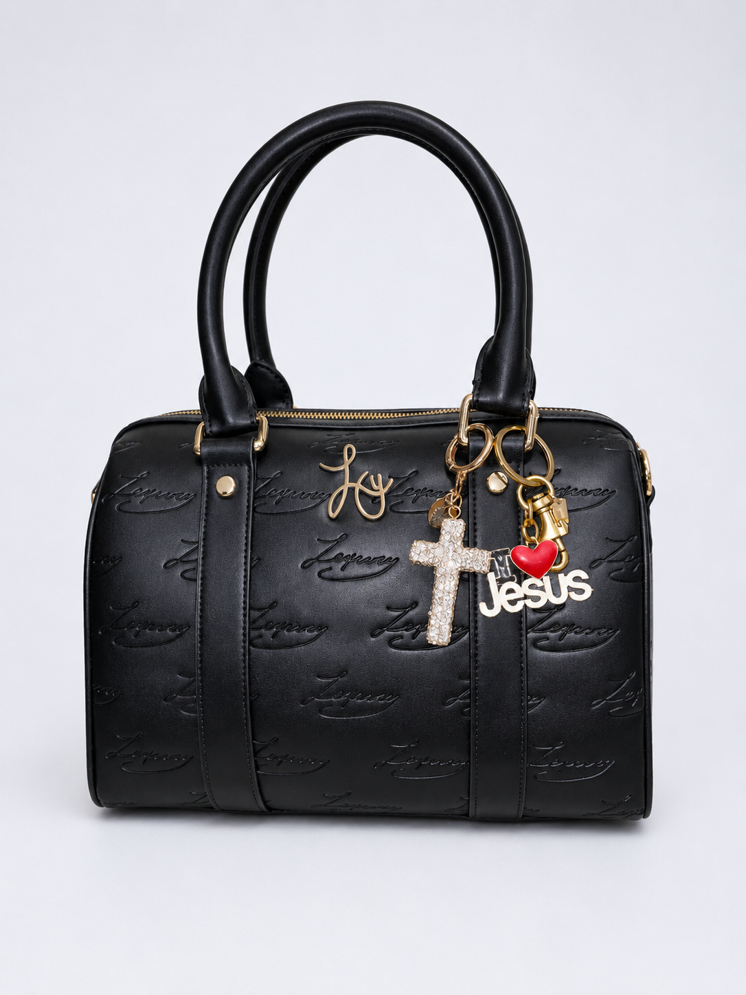 Black handbag with gold hardware, charms including a cross, heart, and the word Jesus, and the name Joy written repeatedly on the surface.