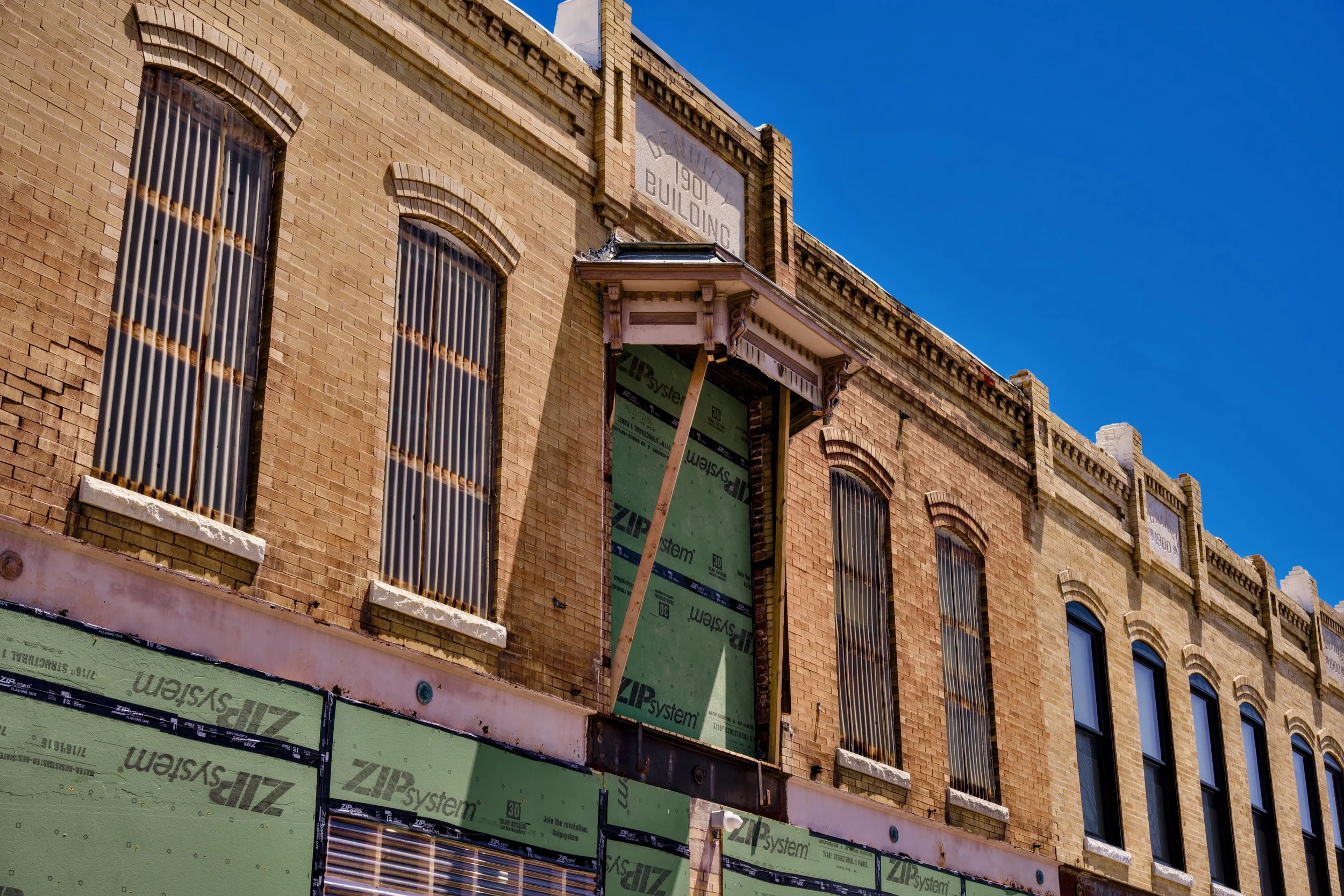 A brick building under construction with windows covered by metal bars, and the top sign indicating it was built in 1901 in Cincinnati; part of the building appears to be incomplete with green construction materials and support beams visible.
