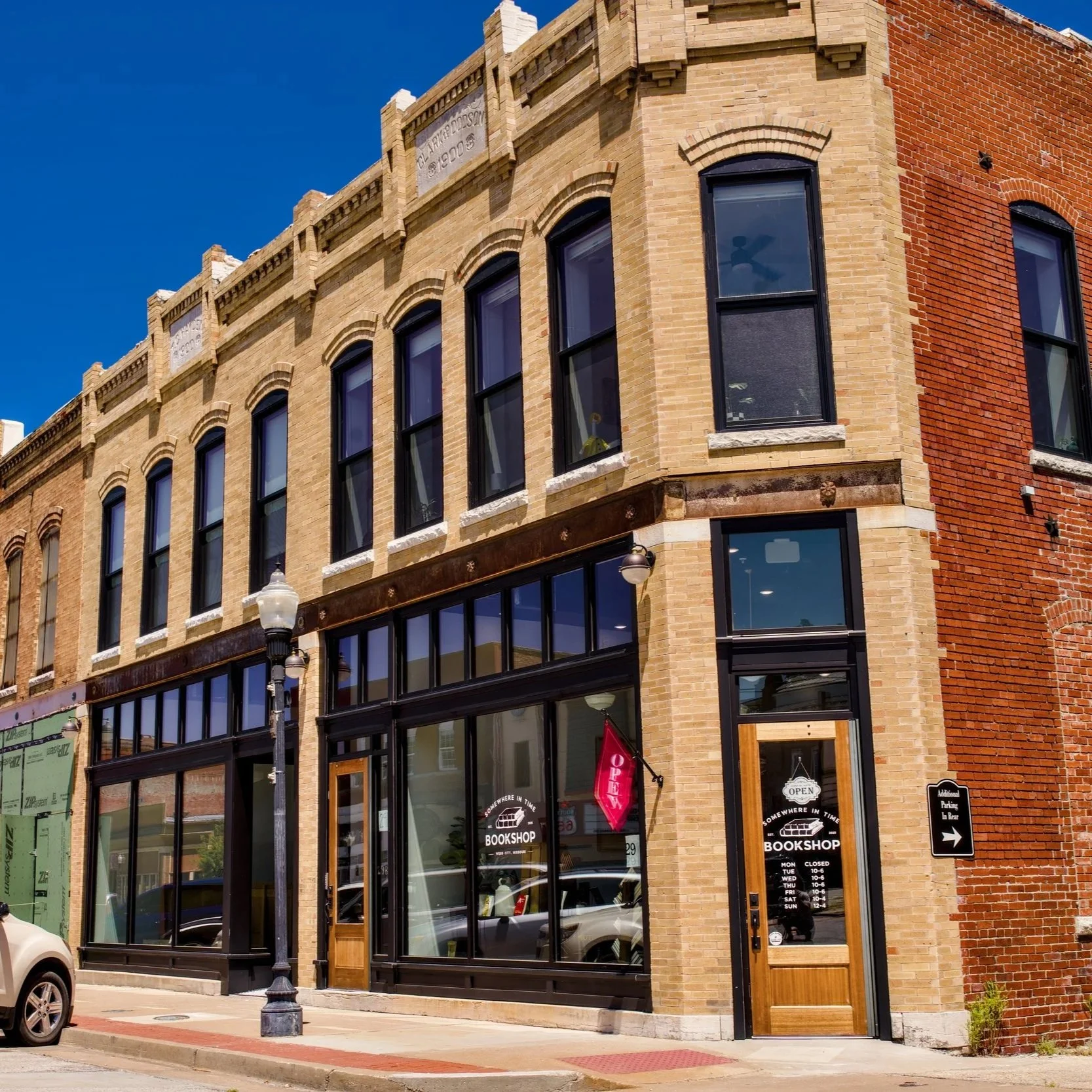 Corner view of a brick building housing a bookstore, with large glass windows and an 'Open' sign on the door, under a clear blue sky.
