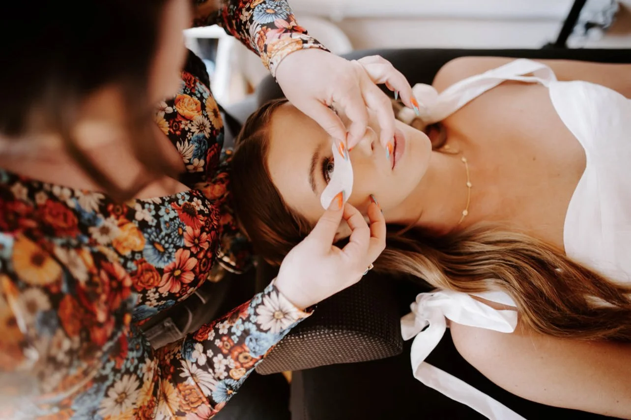 A woman getting her eyelash extensions done by a technician in a salon.