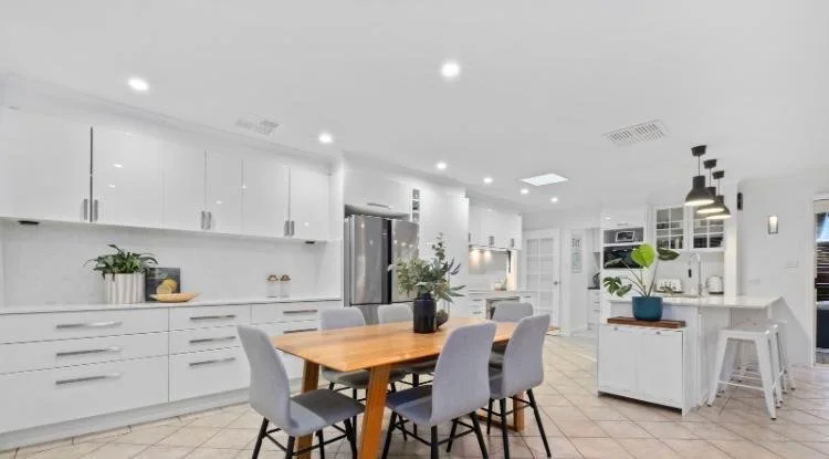 Modern open-plan kitchen and dining area featuring professional interior painting and plastering, smooth white cabinetry, and a clean contemporary finish by Canberra painters.