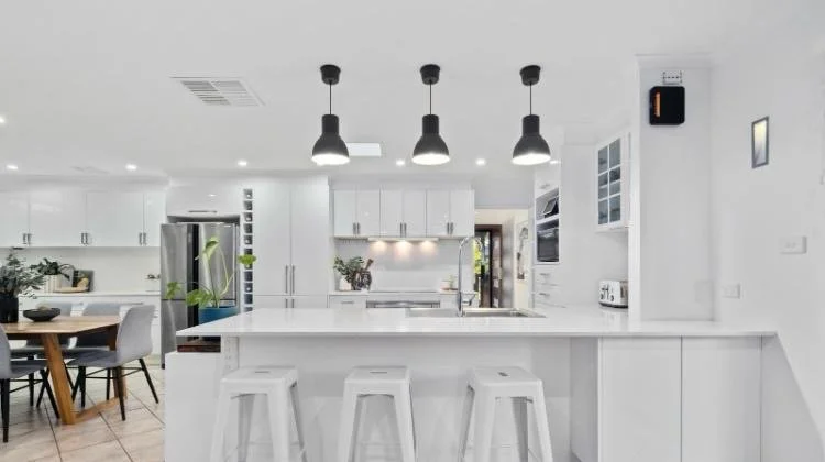 Freshly painted modern white kitchen with island, pendant lights, and dining area in a Canberra residential renovation.