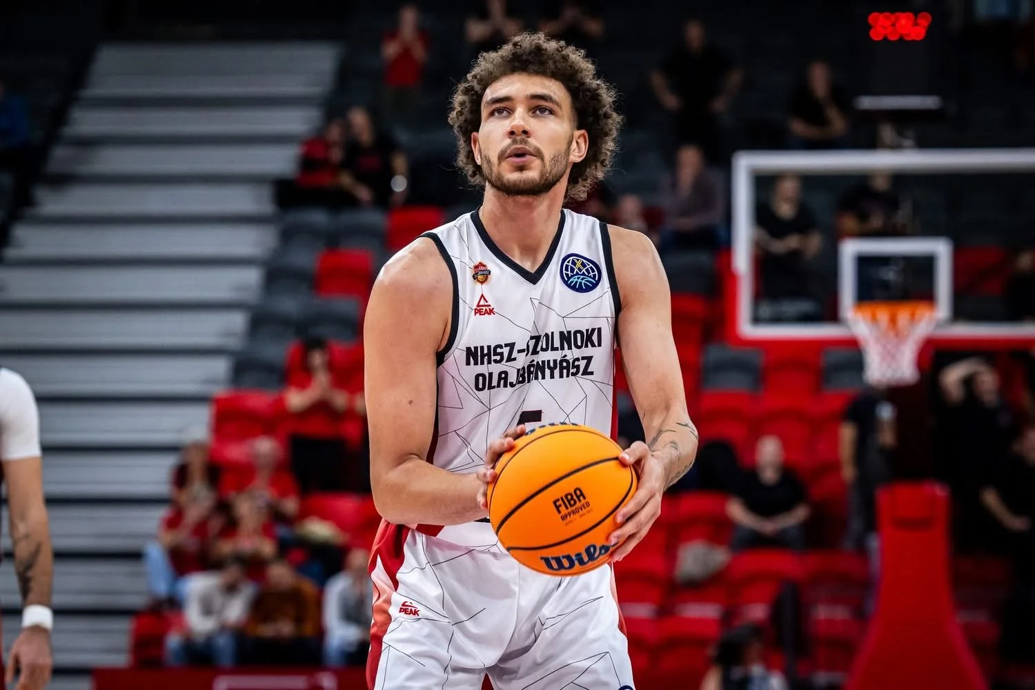 Male basketball player with curly hair, wearing a white jersey holding a basketball during a game.