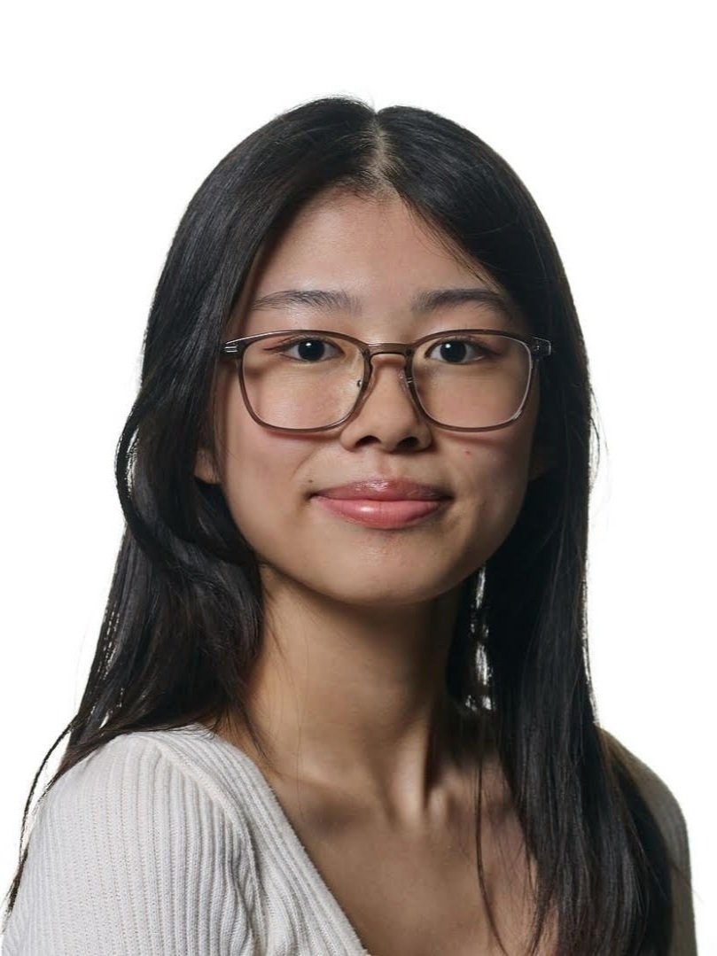 A young woman with long black hair, wearing glasses and a light-colored top, smiling at the camera against a white background.