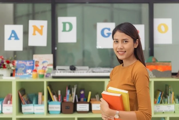 A young woman holding books in a classroom with colorful alphabet posters on the window in the background.