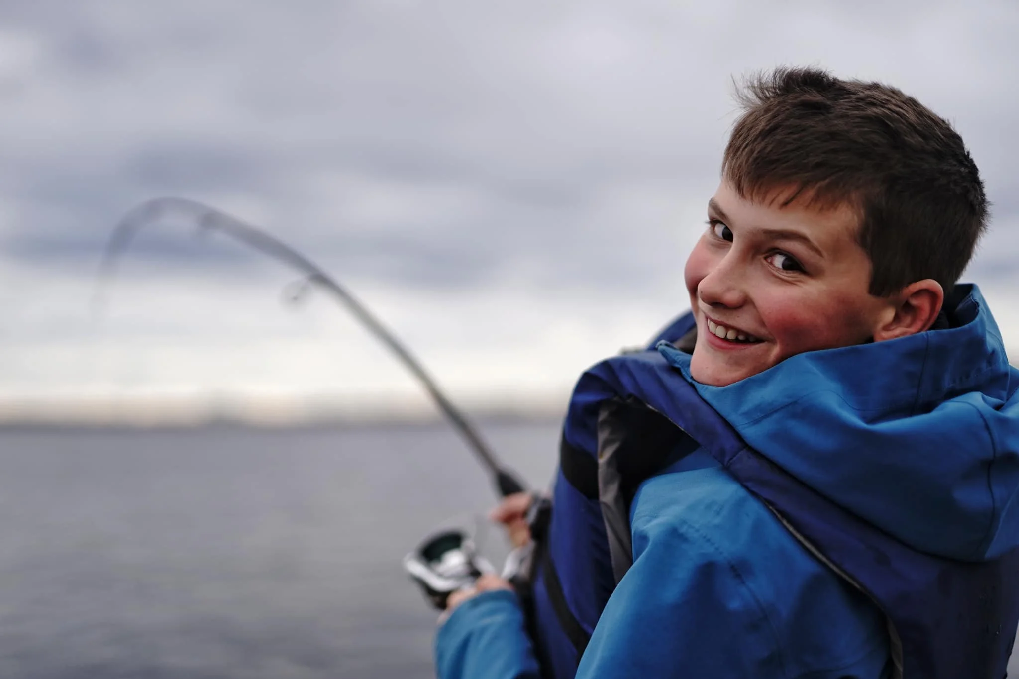 A young boy smiling and fishing on a cloudy day on a body of water in miramichi new brunswick