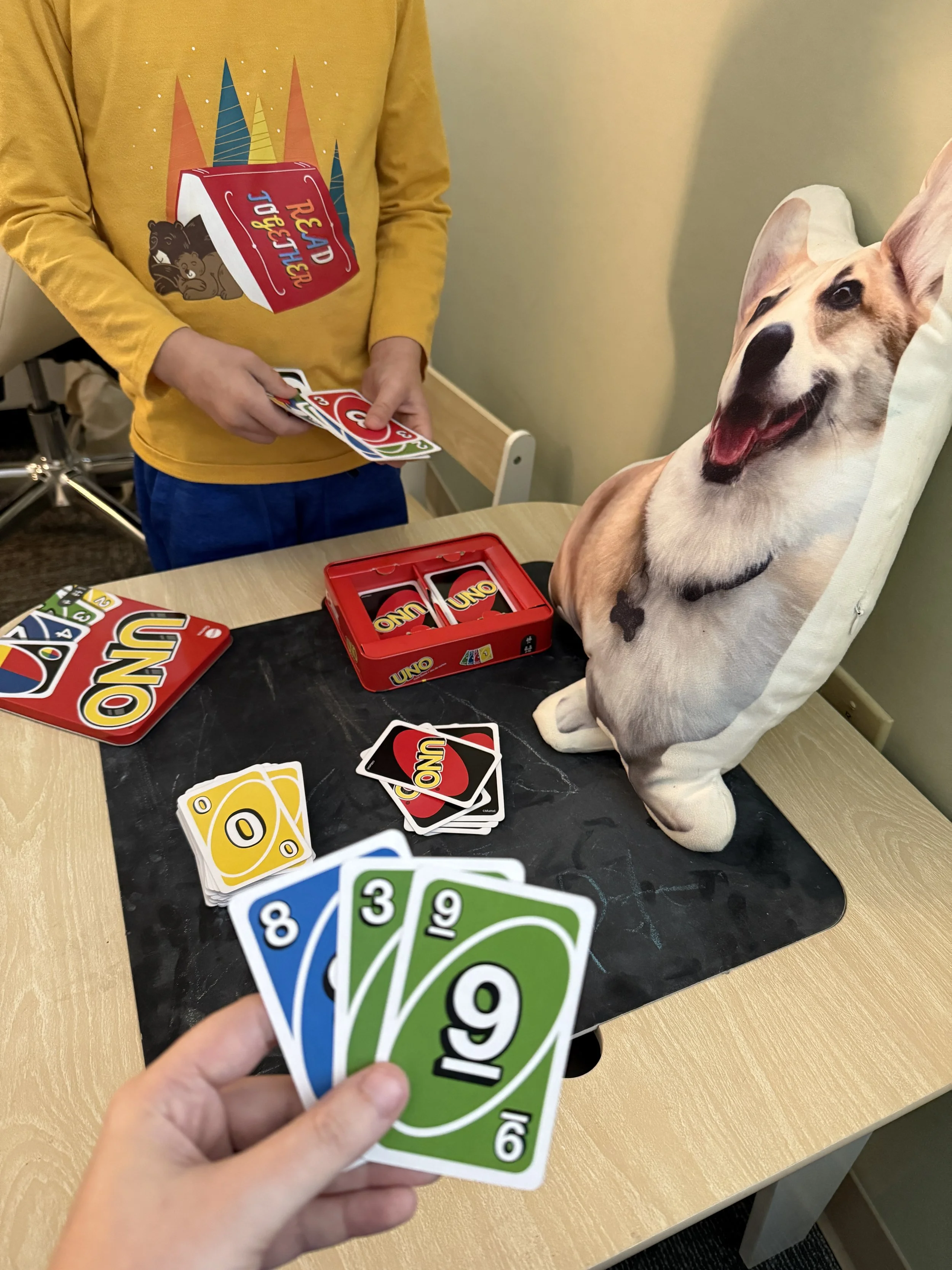 A photo of Dr. Gibon's office environment, designed to help children feel at ease. This photo features a pillow with George, Dr. Gibson's corgi, on it and a game of Uno being played by children.