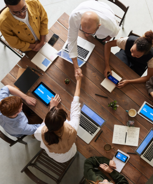 six people around a table where two are reaching across the table shaking hands