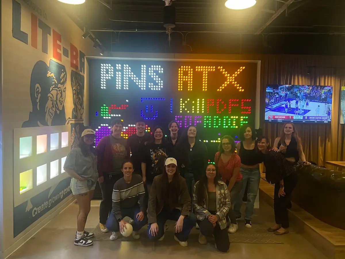 Gay women pose for a picture in front of the Pins Mechanical Co sign in Austin at a Sapphic Weekly ATX hangout