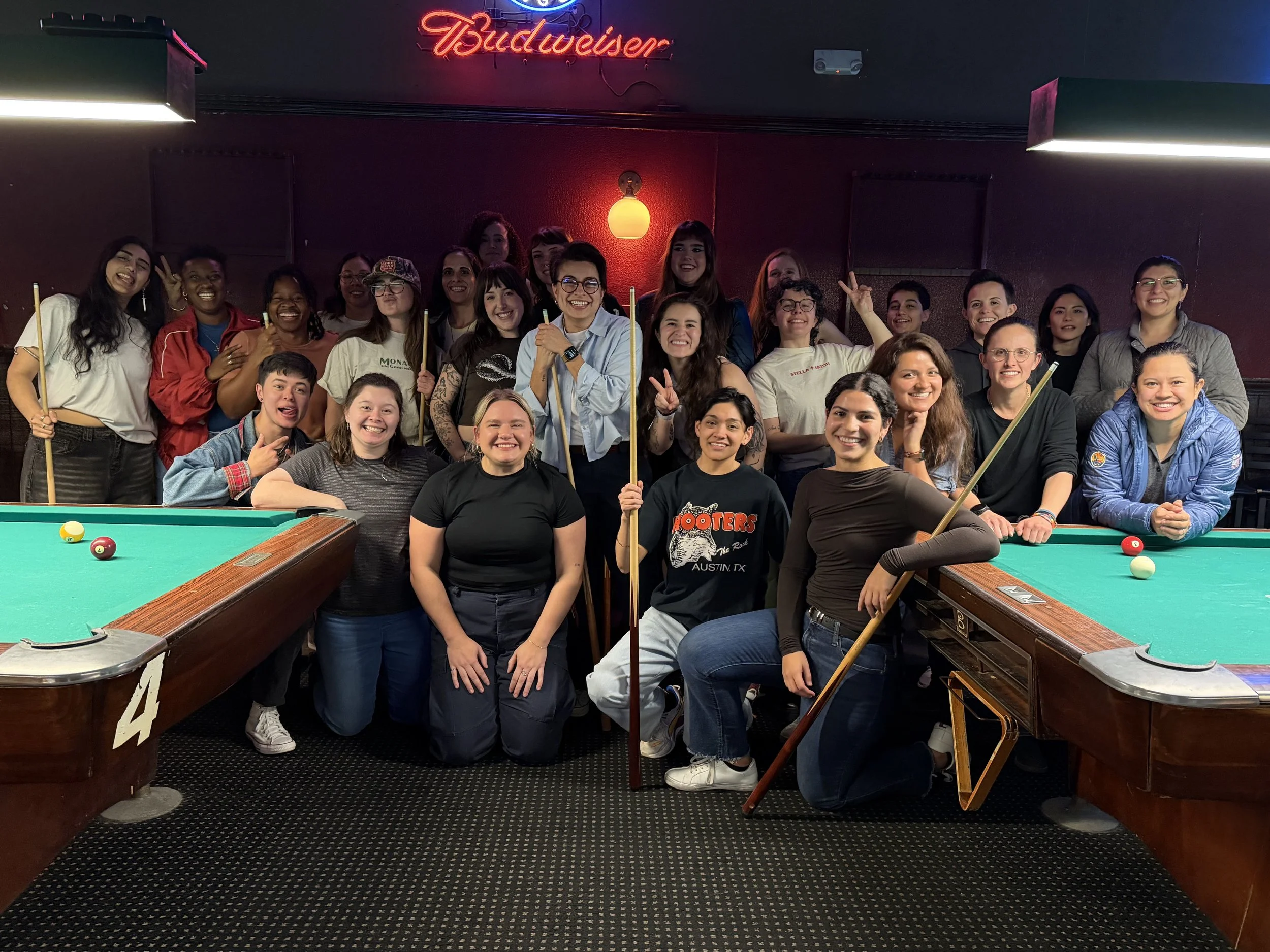 Queer women with pool sticks posing for a picture at the Warehouse in South Austin at an event hosted by Sapphic Weekly ATX