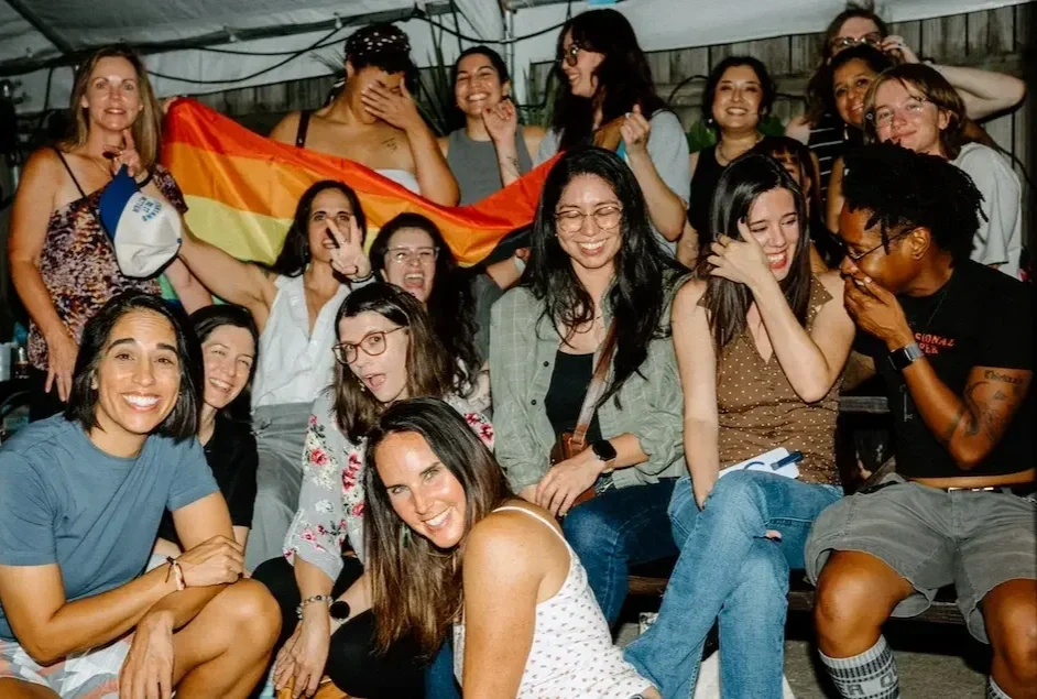 Sapphic women holding up the gay flag at a queer hangout in Austin