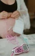 A woman with an unbuttoned shirt exposing her pregnant belly, a pink toy, and a blood glucose meter on a white bed.