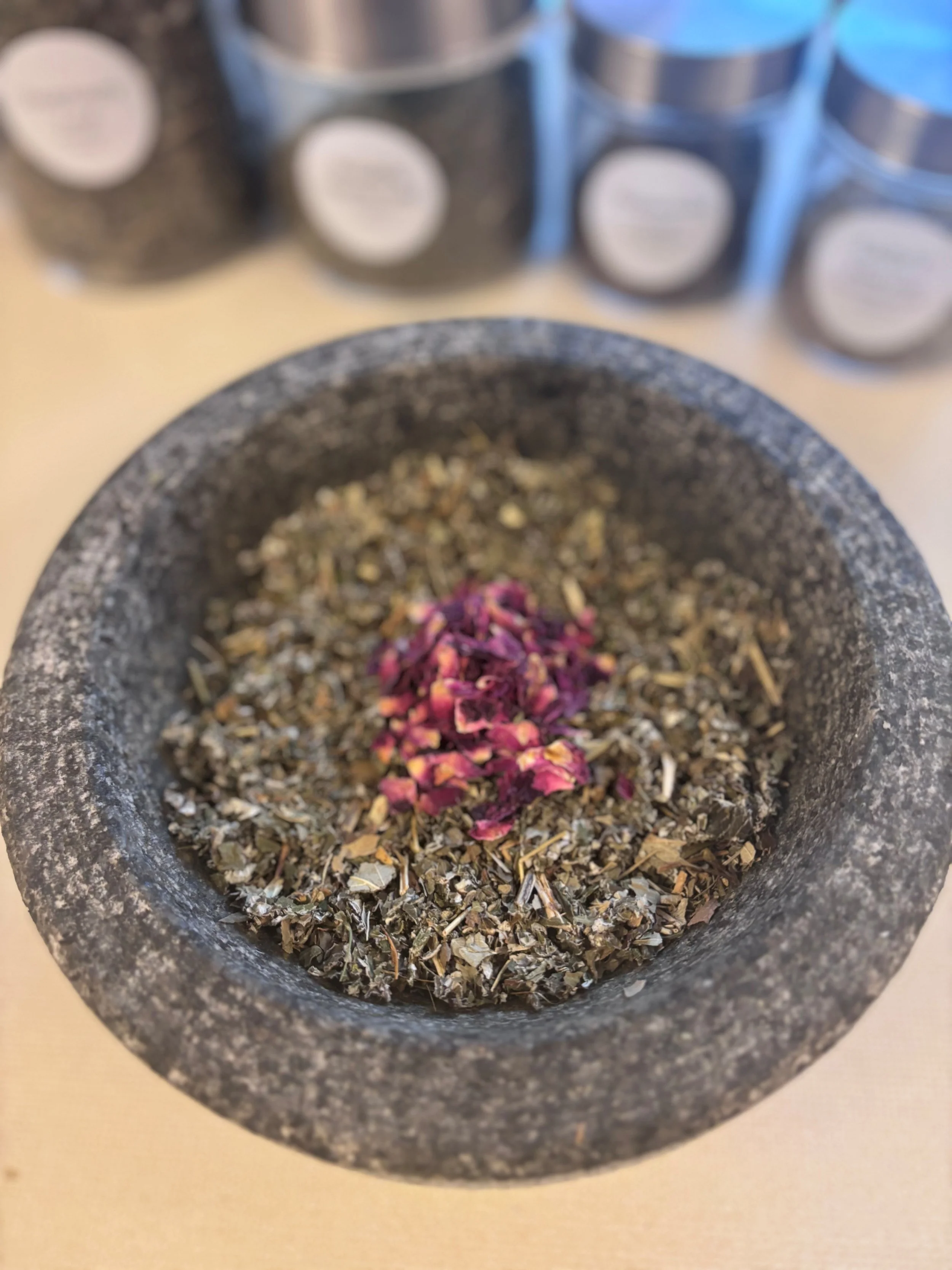 Ground herbs and dried rose petals in a mortar, with spice jars in the background.
