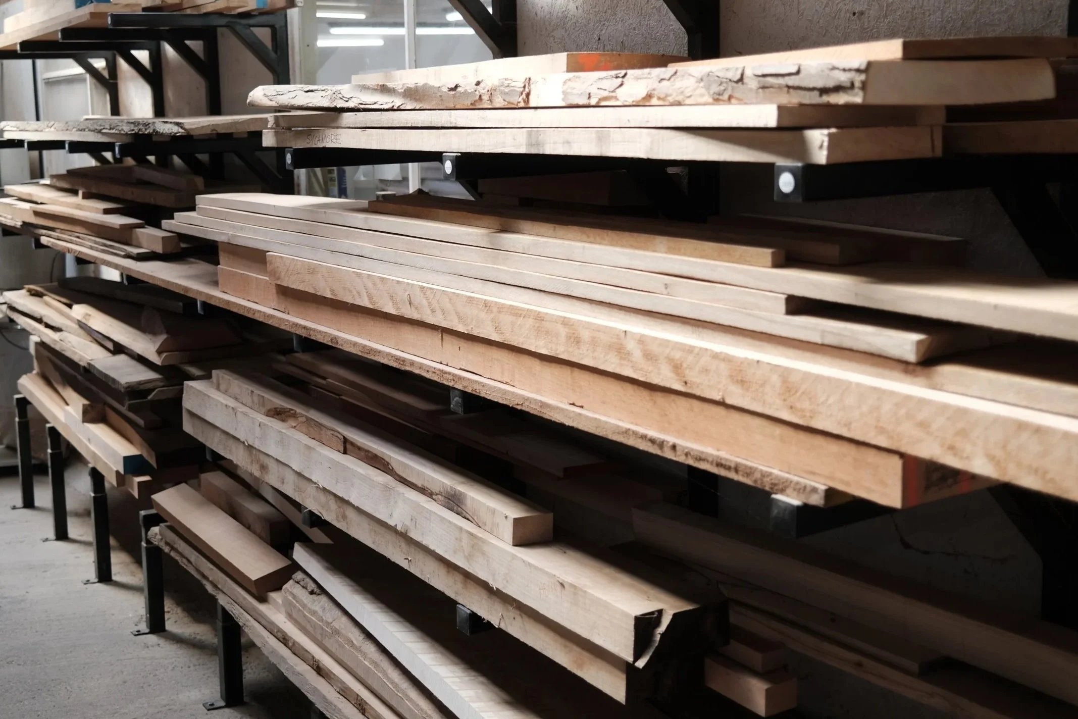Stacked wooden planks and beams on metal shelves in a workshop.