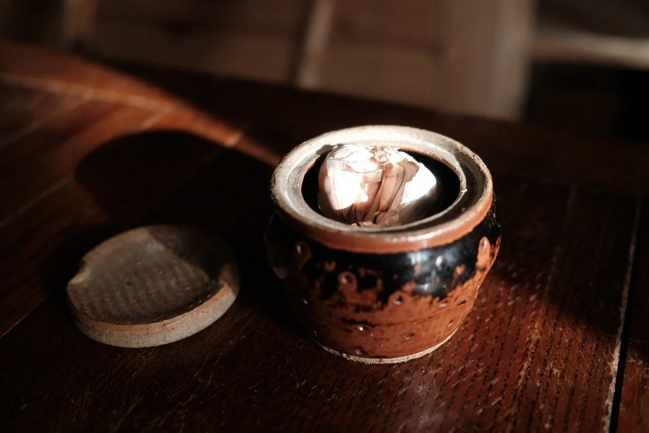 Hand-thrown tenmoku glazed ceramic pot with raw clay lid, open with garlic inside — made by Henry Crabb, West Cornwall