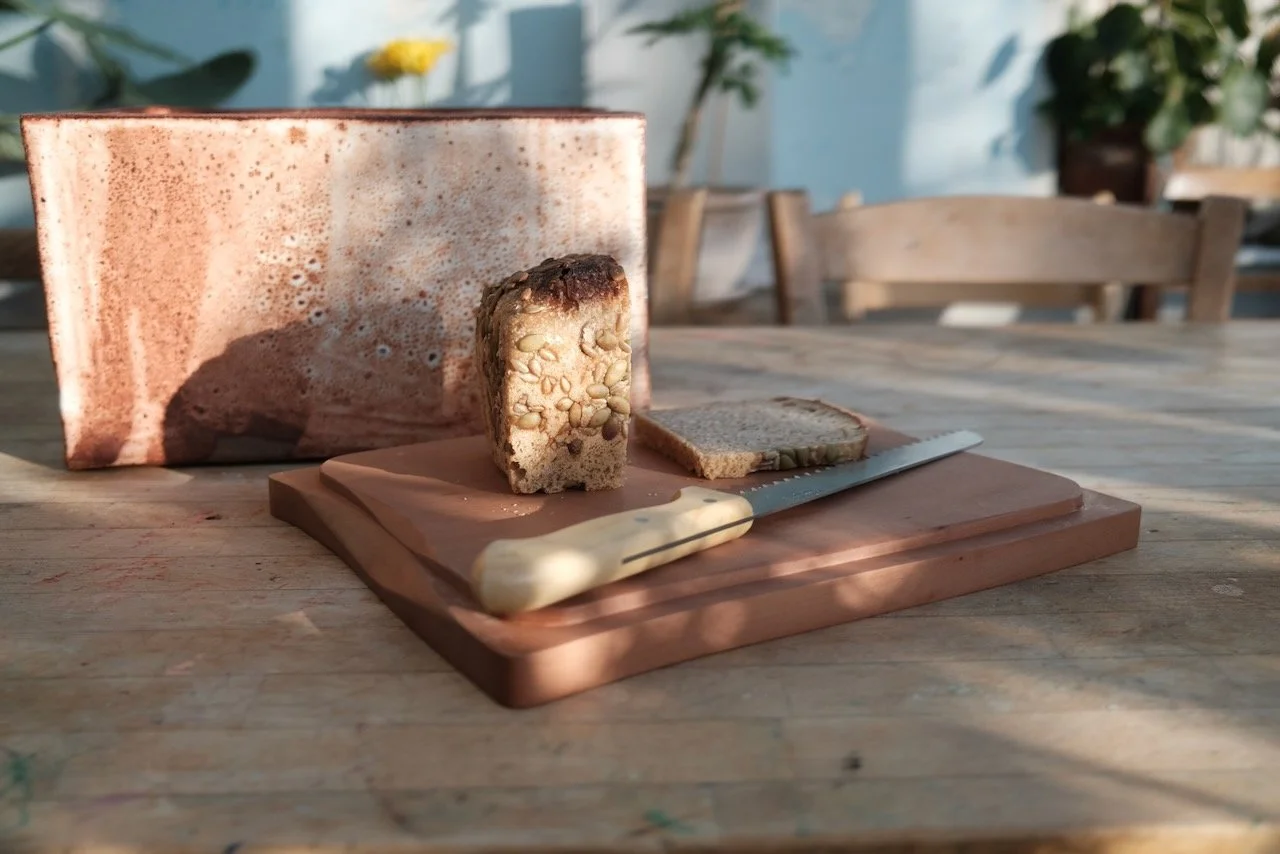Handmade bread bin in shino-glazed Cornish clay with Swiss pear wood cutting board lid in use — made in collaboration with Leach Pottery, St Ives, by Henry Crabb