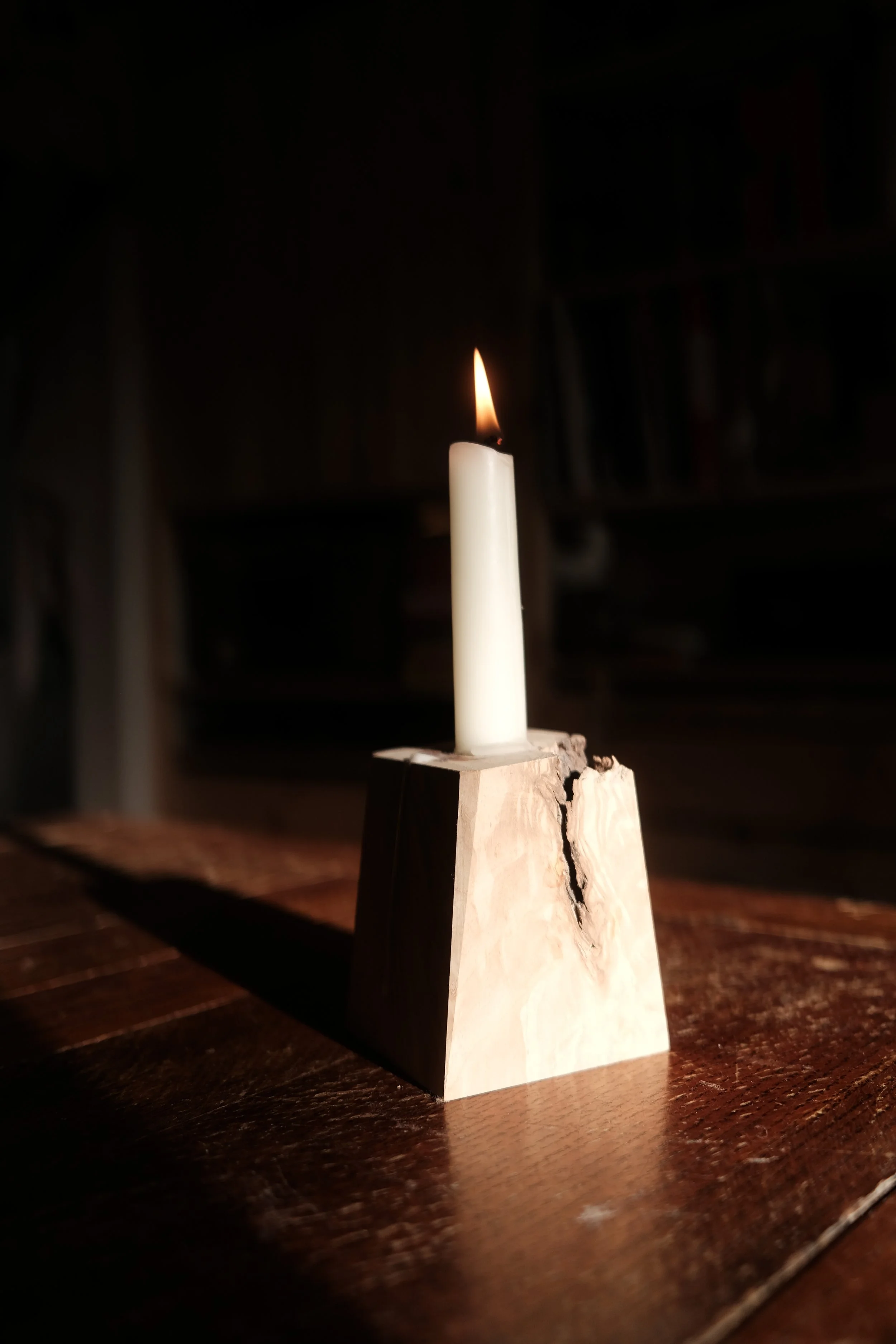 Hand-made wooden candlestick holder with live-edge detail, lit candle, photographed in a darkened workshop — a small object by Henry Crabb