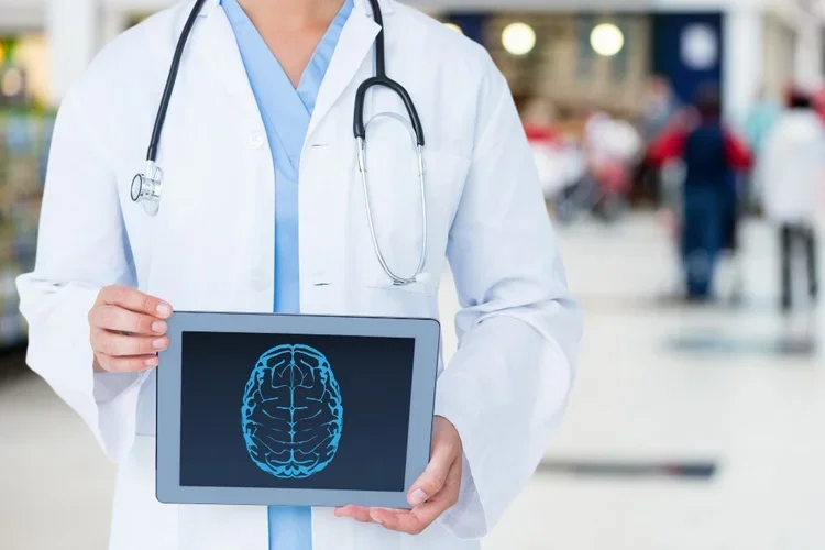Doctor in a white coat and stethoscope holding a tablet displaying a brain scan at a medical facility.