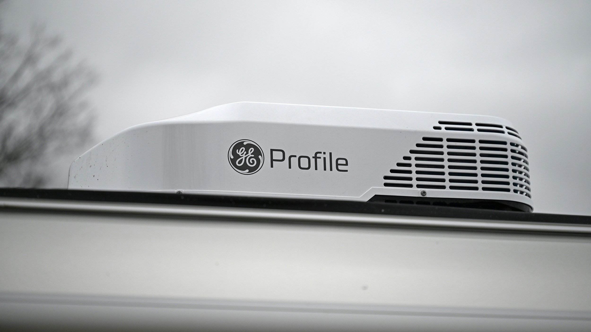 Close-up of a GE Profile kitchen appliance, likely an oven or refrigerator, installed on a white surface with overcast sky in background.