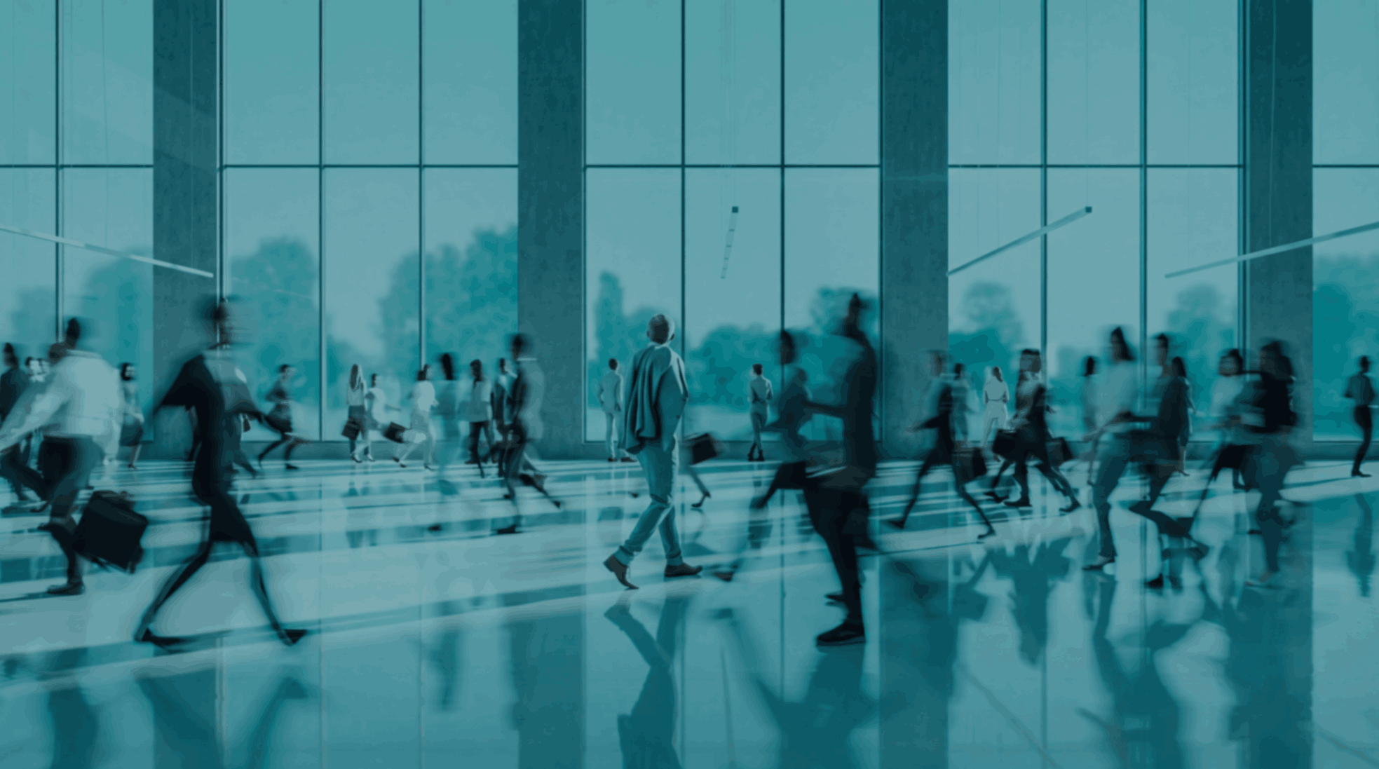 People walking in an airport terminal with large glass windows reflecting trees outside.