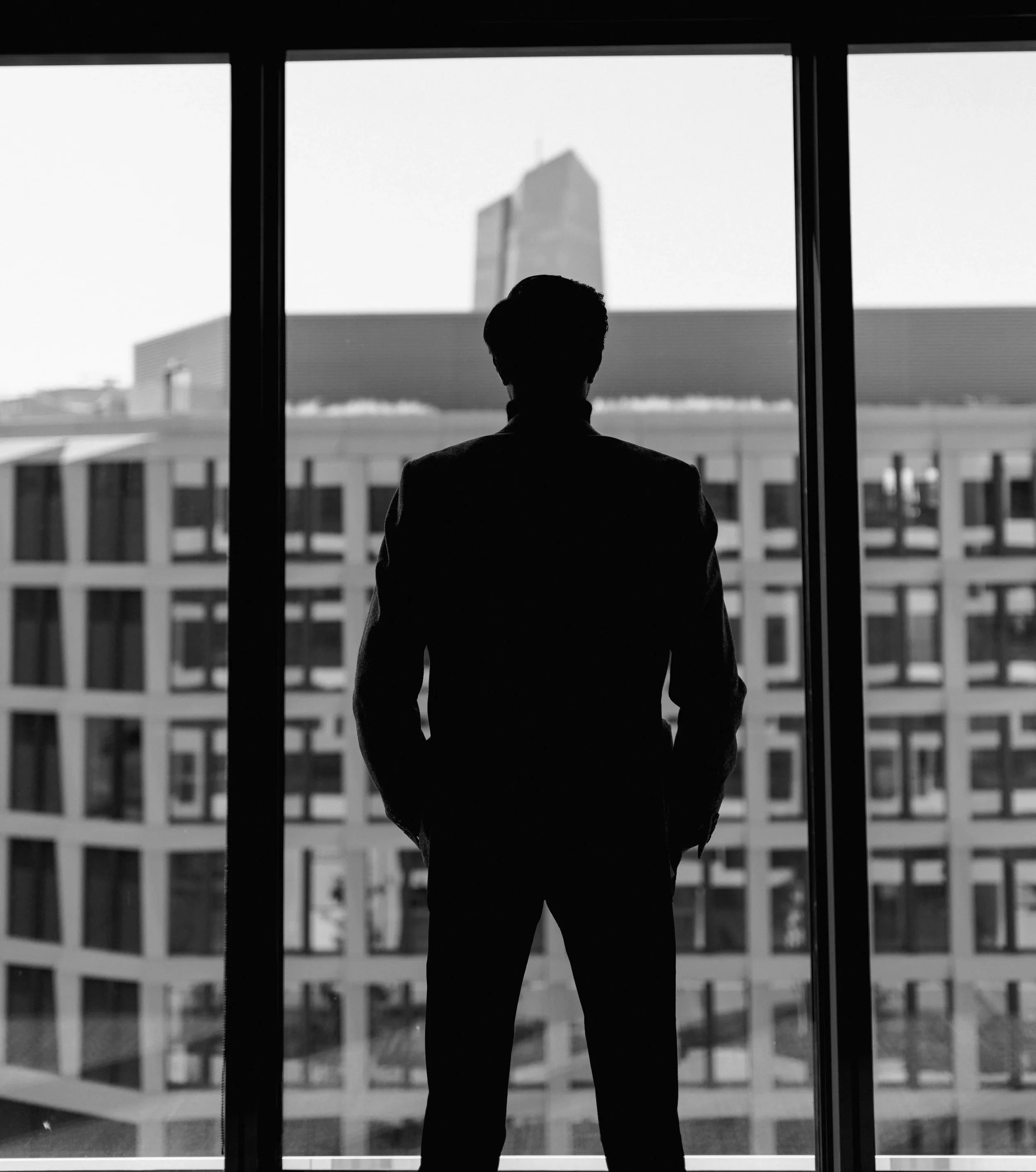 Silhouette eines Mannes, der vor einem Fenster steht, mit Blick auf eine moderne Gebäudeskyline.