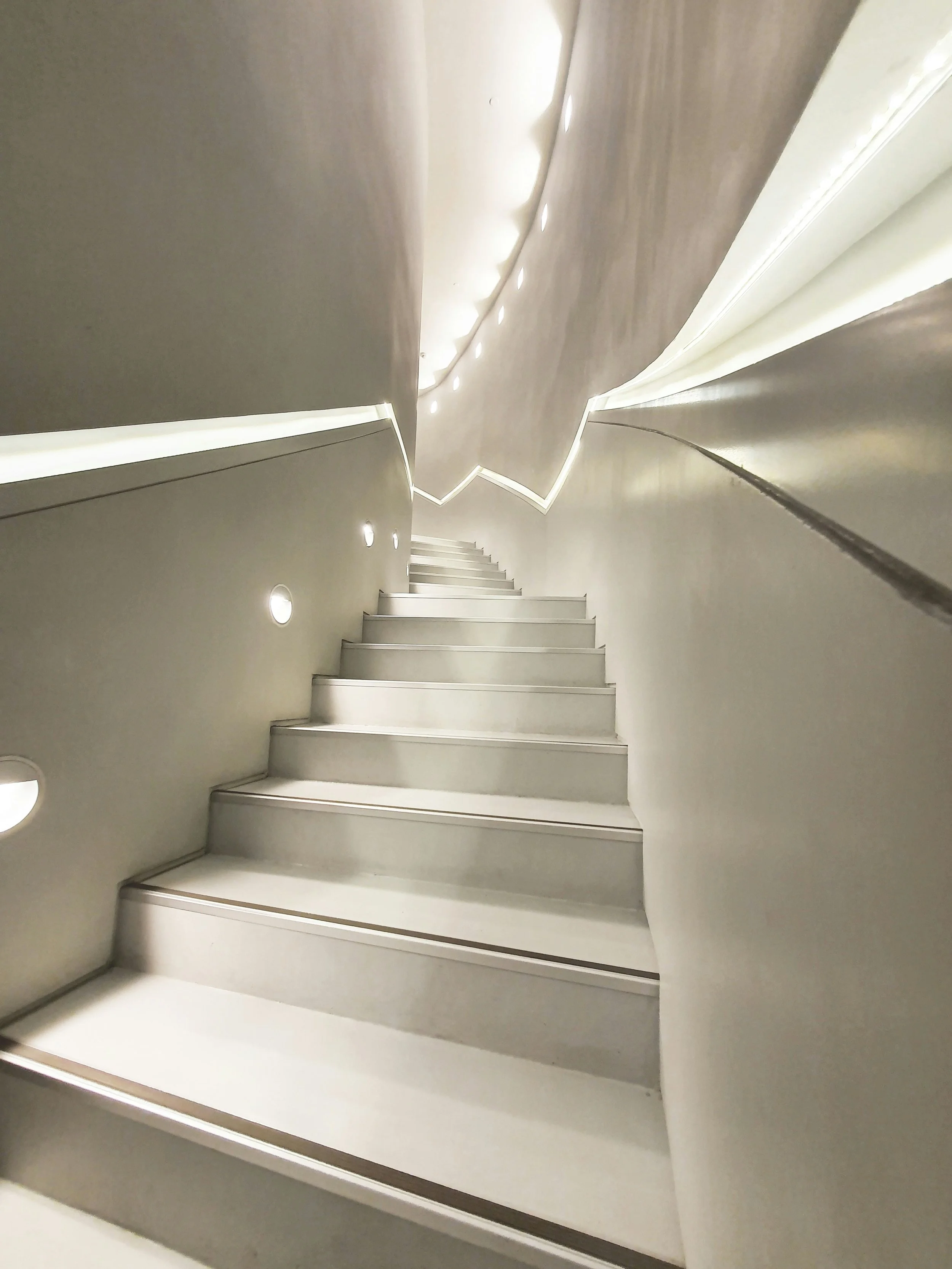 Innenaufnahme einer modernen, weißen Treppe mit LEDs an den Seiten, die nach oben führt.