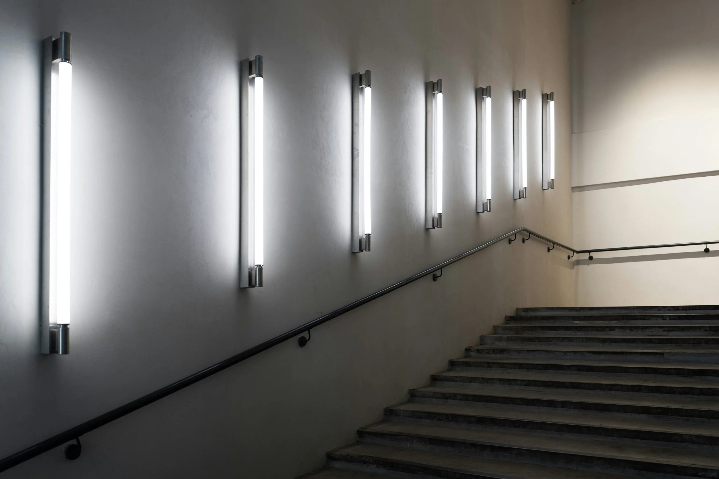 Innenansicht einer Treppe mit Schwarzstahlhandläufen und Wandlampen, helle Wände, modern minimalistischer Stil.