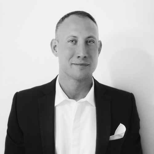 Black and white portrait of a man in a suit with a white shirt and pocket square, looking at the camera.