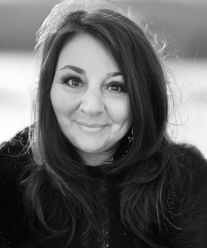 A woman with long dark hair smiling outdoors in black and white.