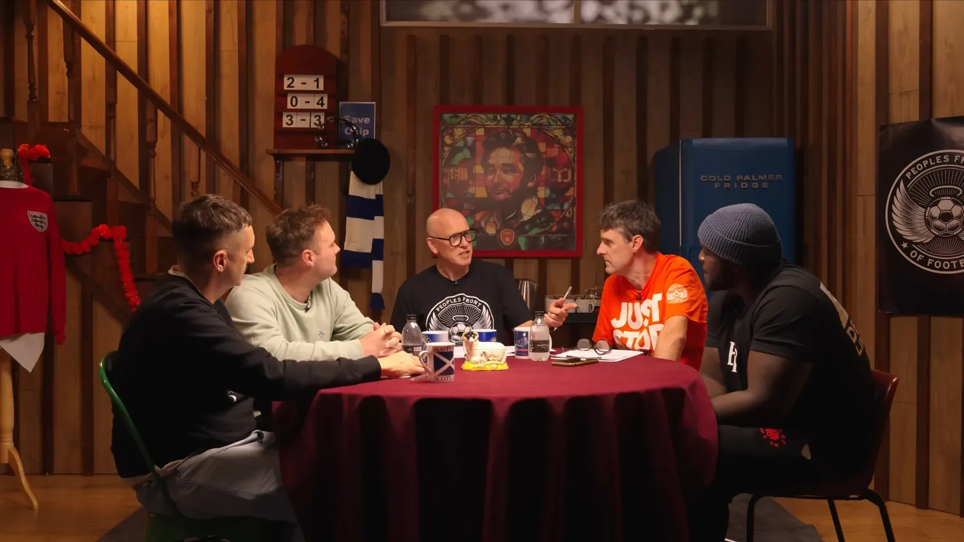 Five men seated around a round table having a discussion in a wooden room decorated with sports memorabilia and artwork.