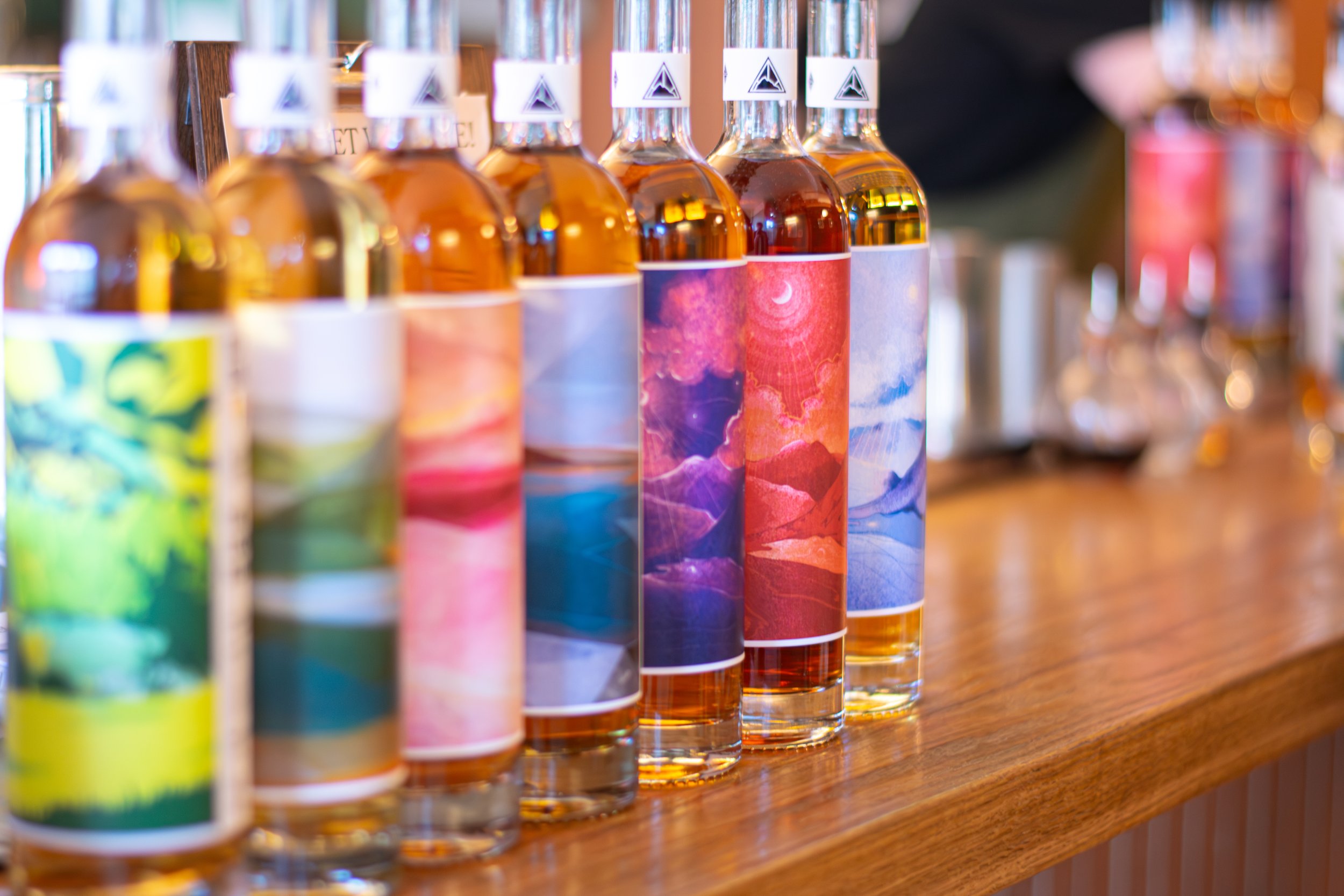 A row of bottles with colorful artwork labels on a wooden shelf.