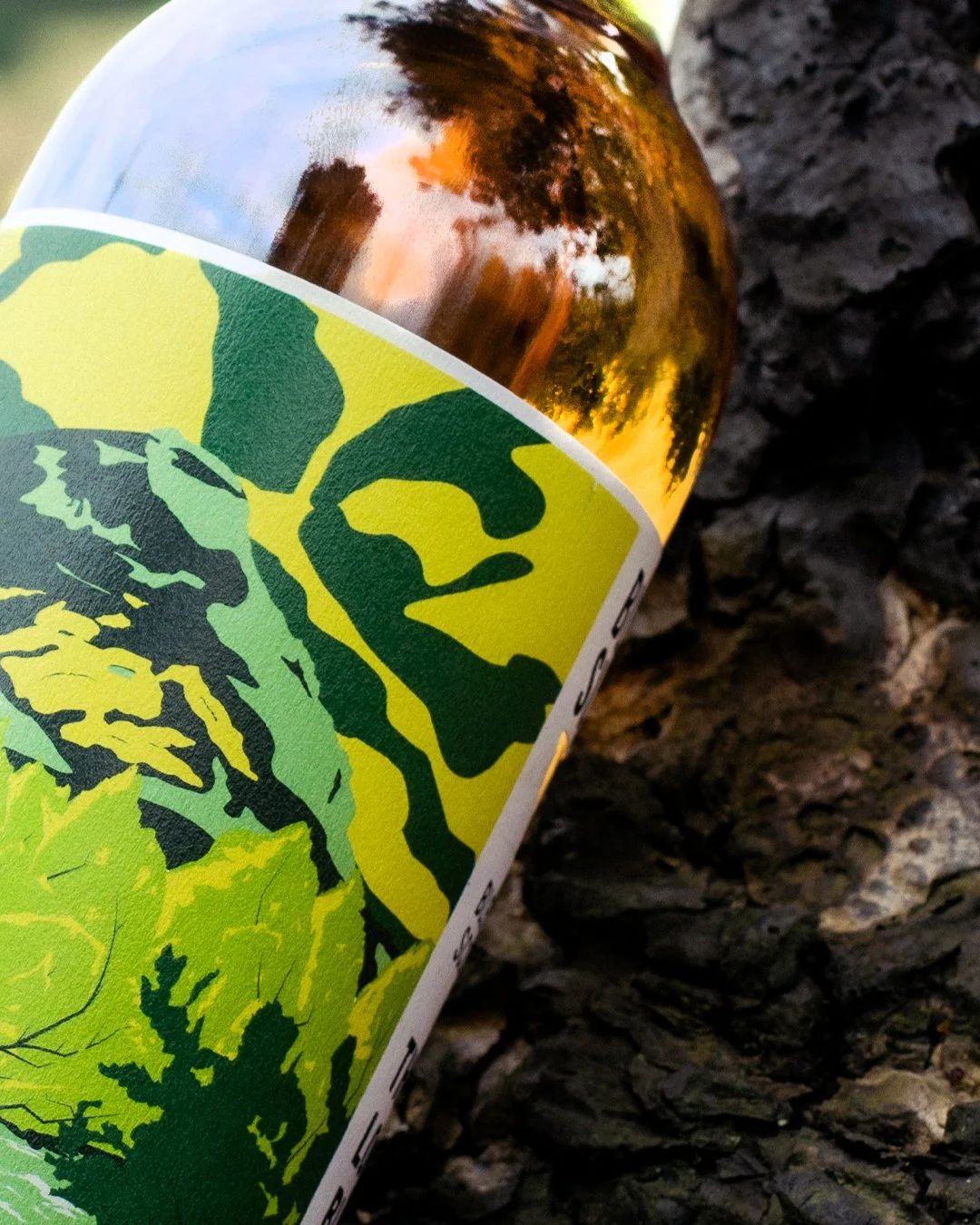Close-up of a bottle with a green and yellow leaf-patterned label, placed on a dark, textured surface resembling bark.