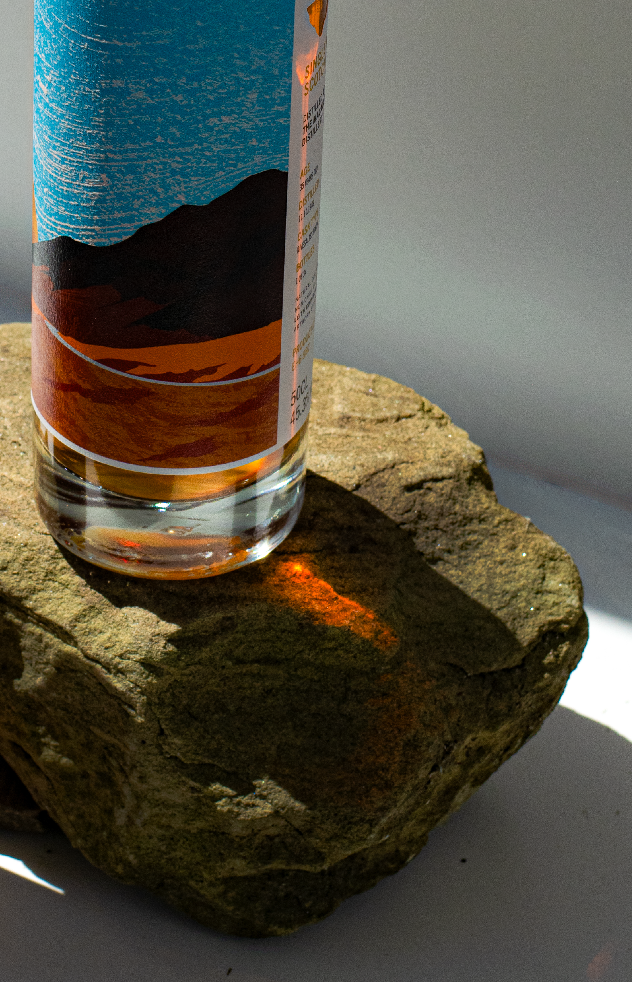 A bottle of Blind Summit Macallan, displayed on a rock with sunlight creating a reflection on the glass and a shadow on the stone.