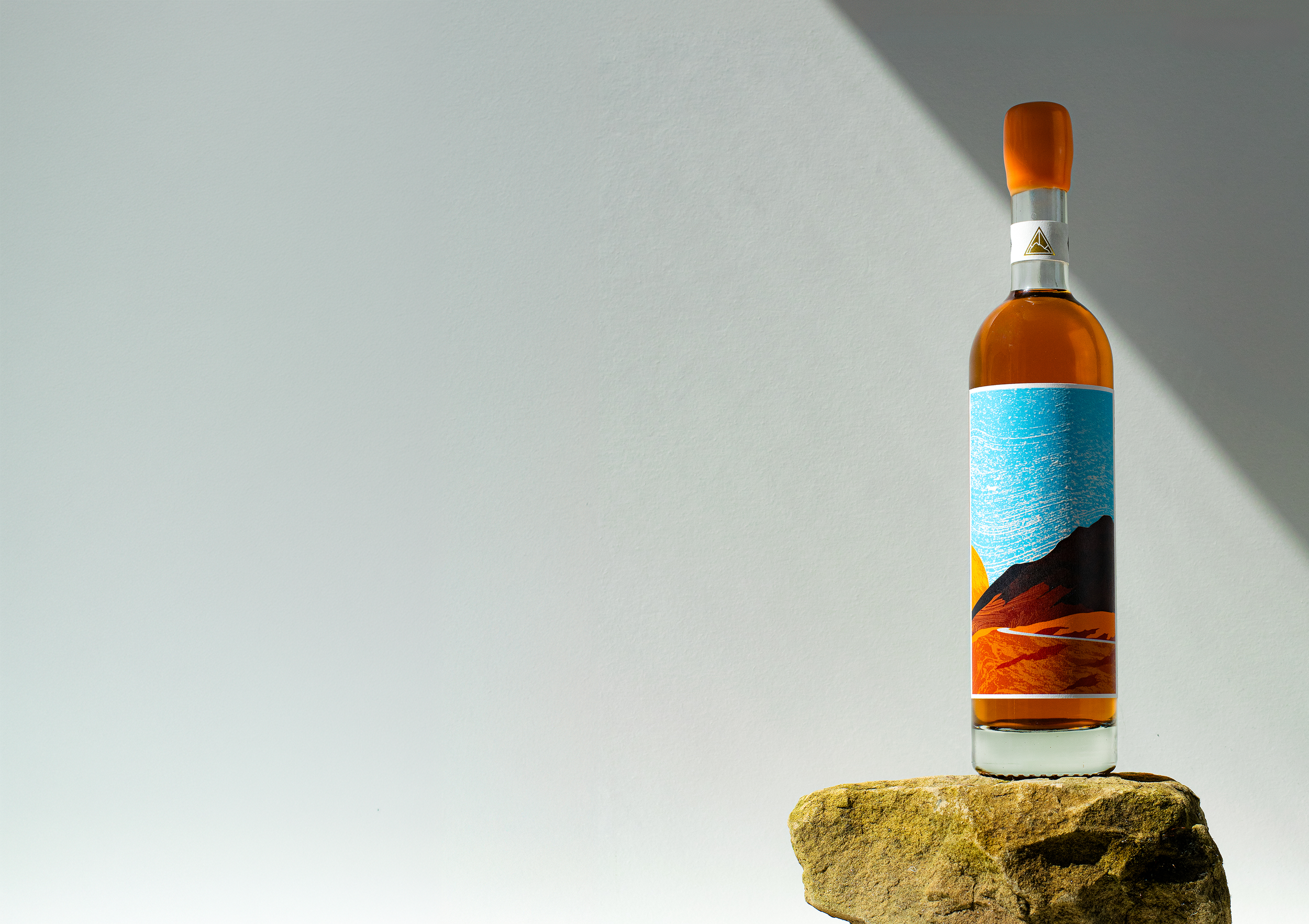 The Blind Summit Macalan Riveseltas Wine finish being displayed on a light rock with a grey gradient background and sunlight highlighting the whisky in the bottle.