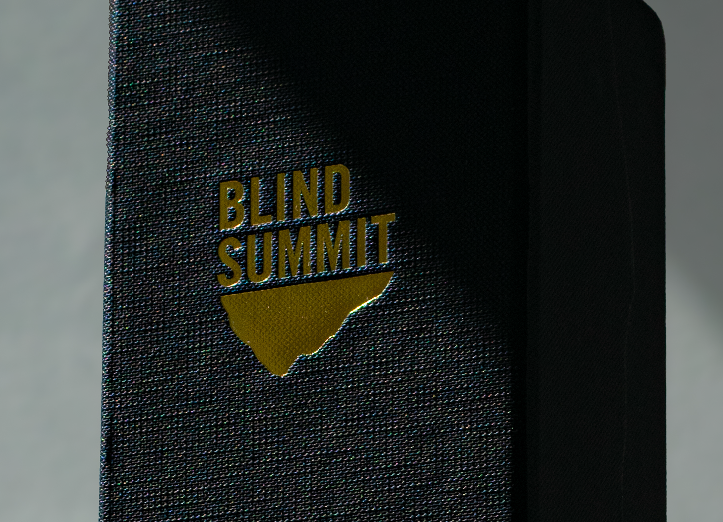 Close-up of a black foiled badge with the words 'Blind Summit' featuring a mountain, attached to a textured box.