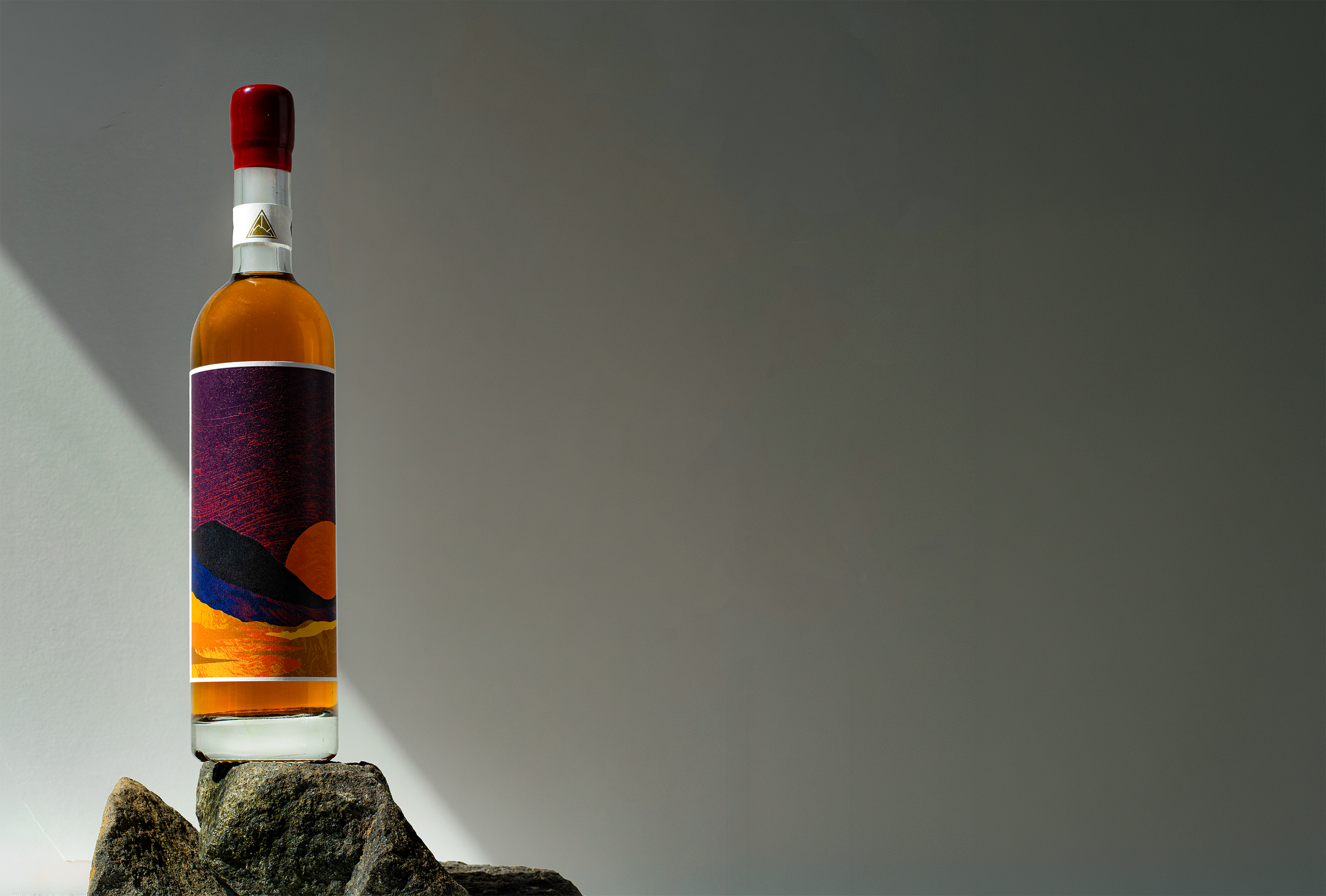 The Blind Summit Macalan Barbados Rum finish being displayed on a dark rock with a grey gradient background and sunlight highlighting the whisky in the bottle.