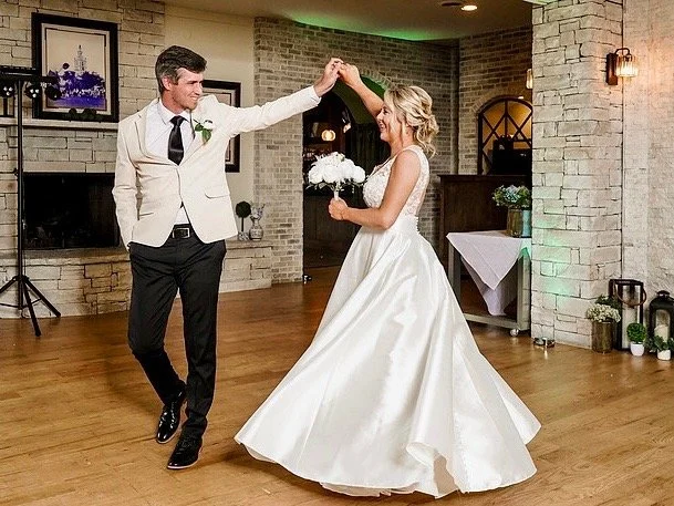 Bride and groom dancing at wedding reception indoors, smiling and holding hands.