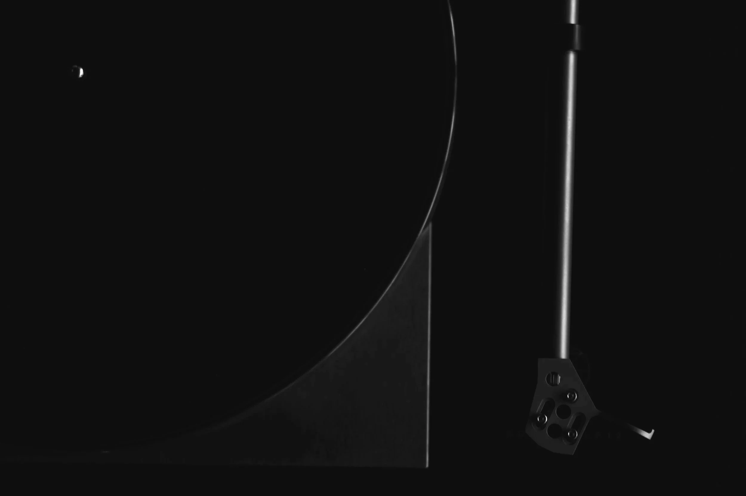 Close-up of a turntable tonearm and platter against a black background.