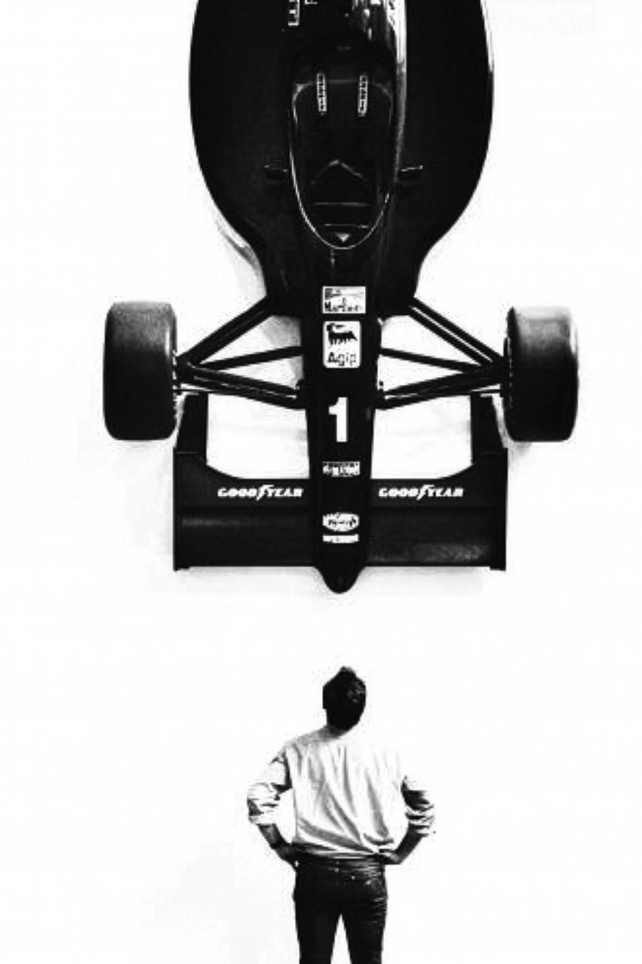 A man stands with hands on hips, looking at a large black race car mounted upside down on a wall.