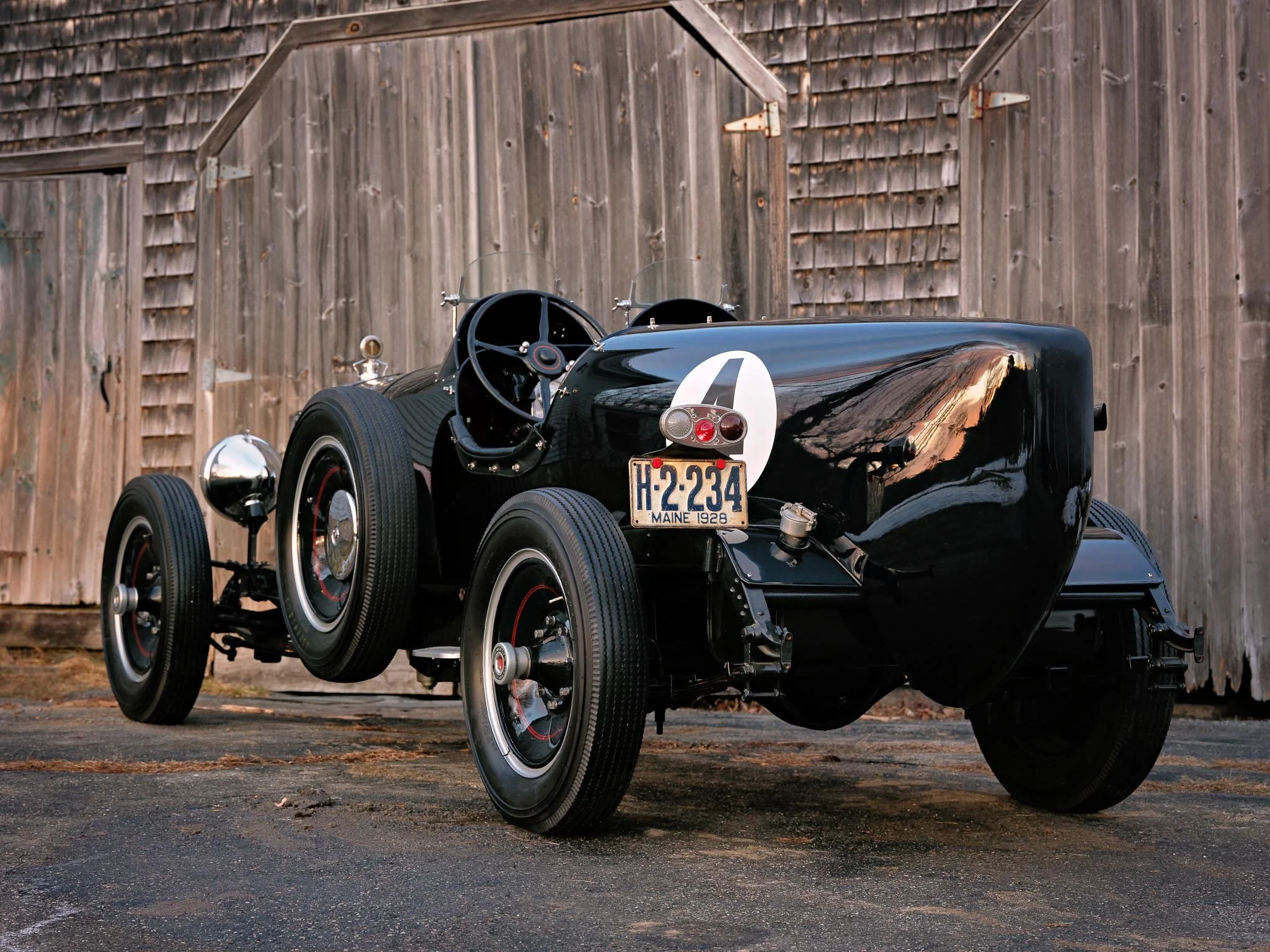 The rear profile of a 1928 Packard Custom Speedster, its tapered tail, exposed suspension, evoking a time when long-distance motoring was both mechanical challenge and romantic pursuit.