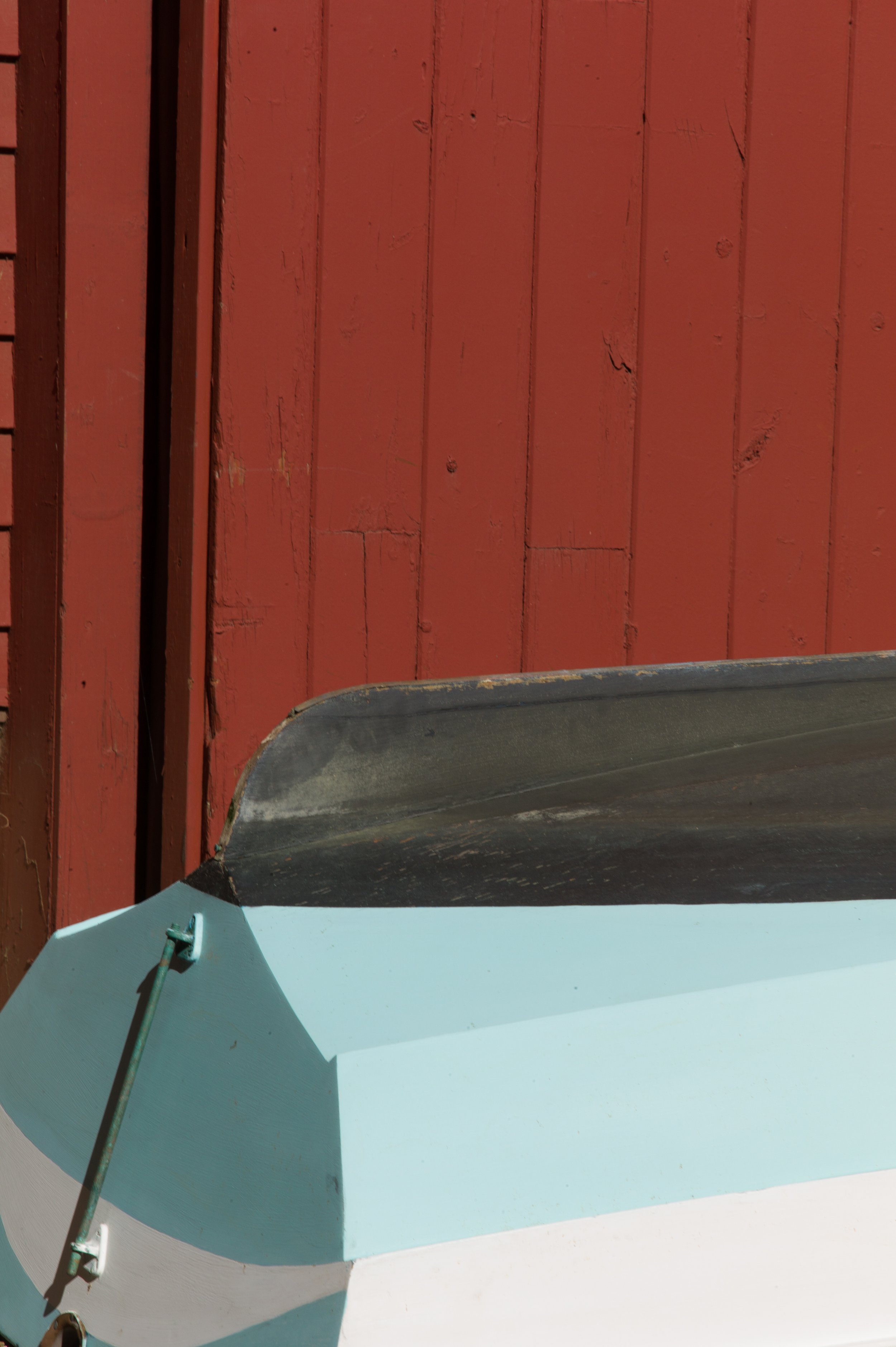 Close-up of a boat with a black rim and light blue sides, positioned in front of a red wooden wall.
