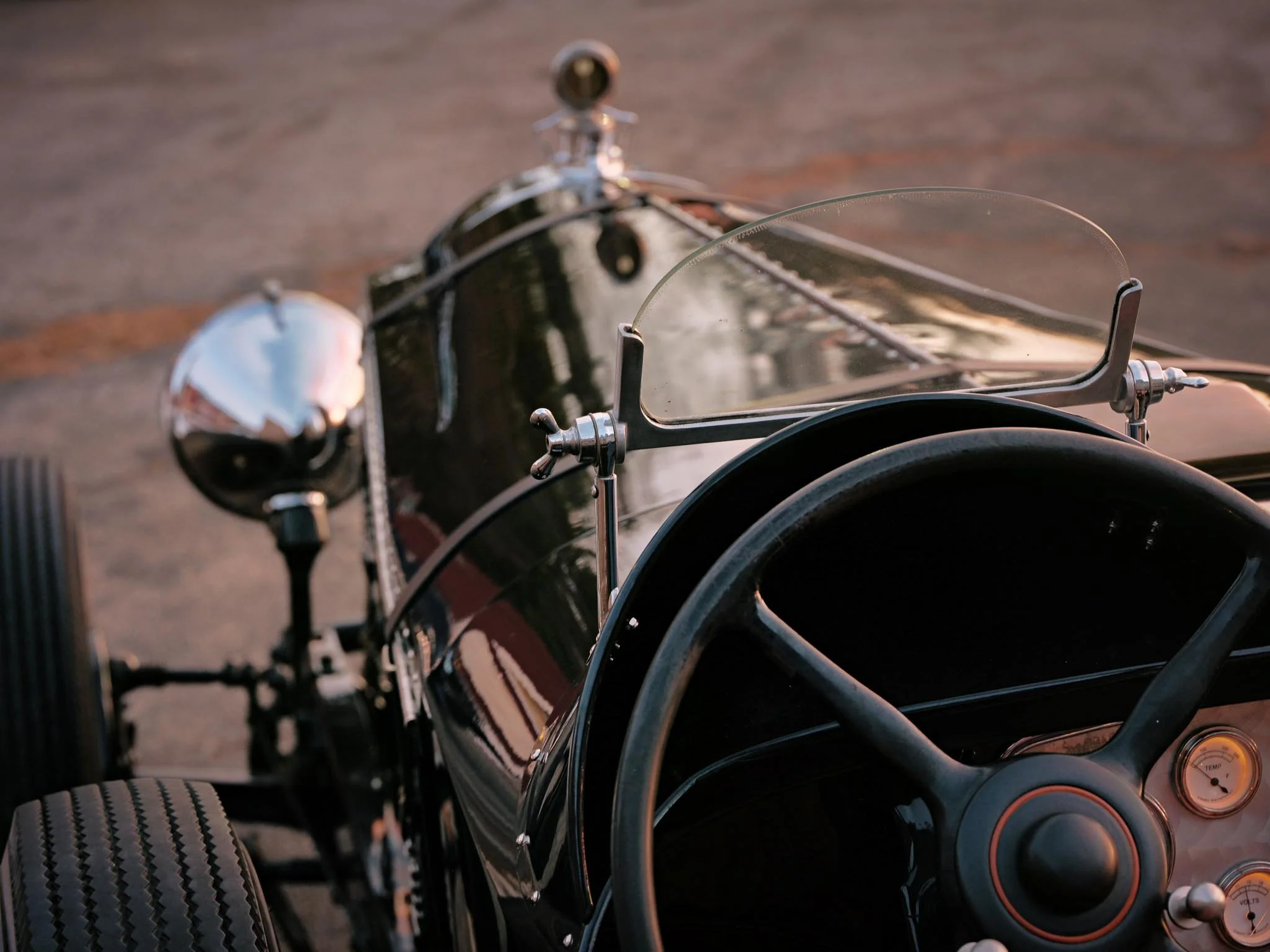 A forward view from the cockpit of a 1928 Packard Custom Speedster, where hand-formed metal, minimal instrumentation, and dual Brooklands windscreens speak to an era when driving demanded both skill and attentiveness.