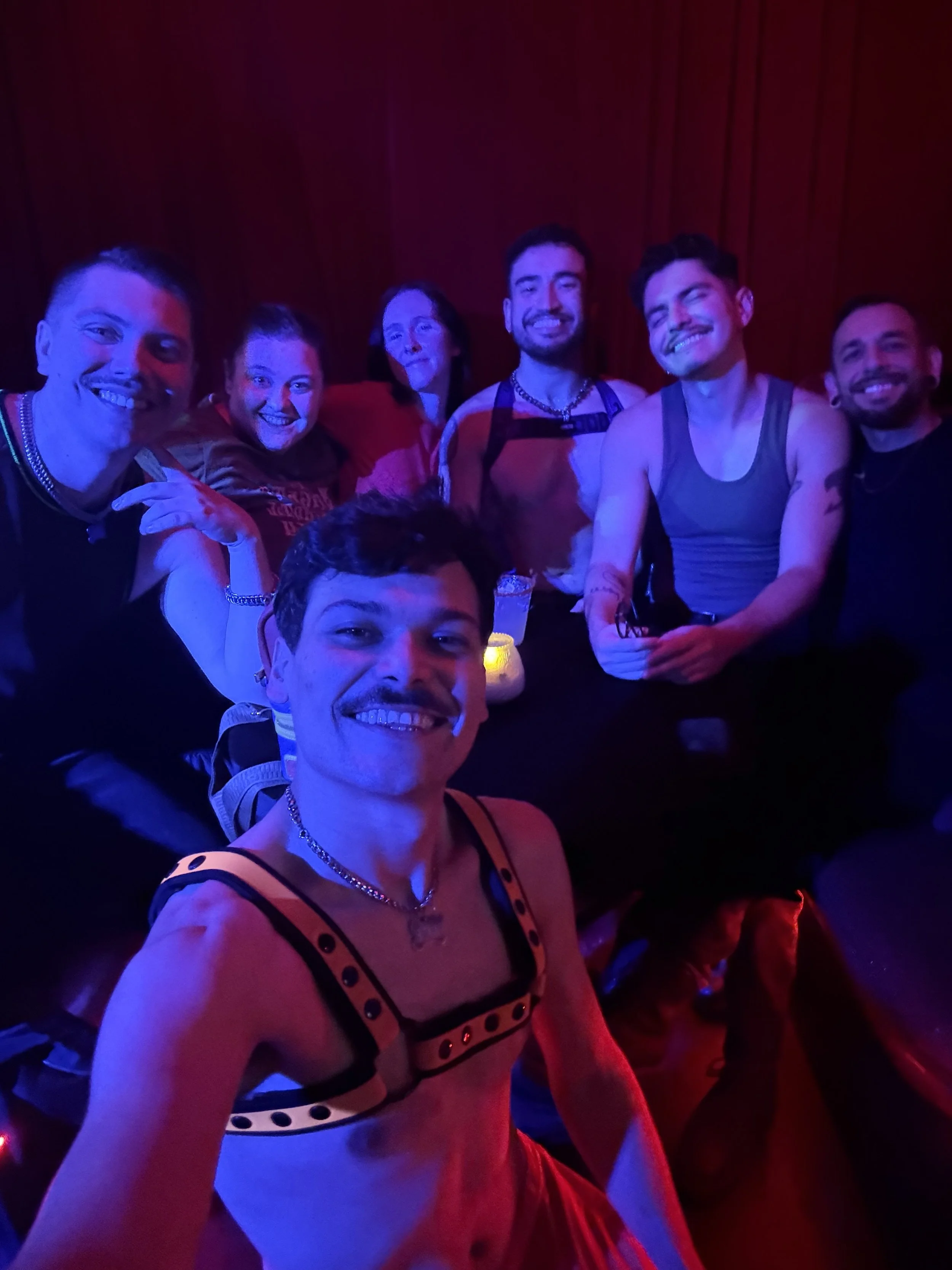 Group of friends taking a selfie at a party with colorful lighting, some are smiling and wearing casual clothes.