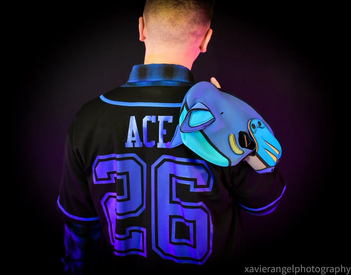Back of a person wearing a black sports jersey with the name 'ACE' and the number '26' illuminated in neon colors. The person is holding a colorful, stylized backpack designed to resemble a cartoon animal head, featuring vibrant blue, purple, yellow,