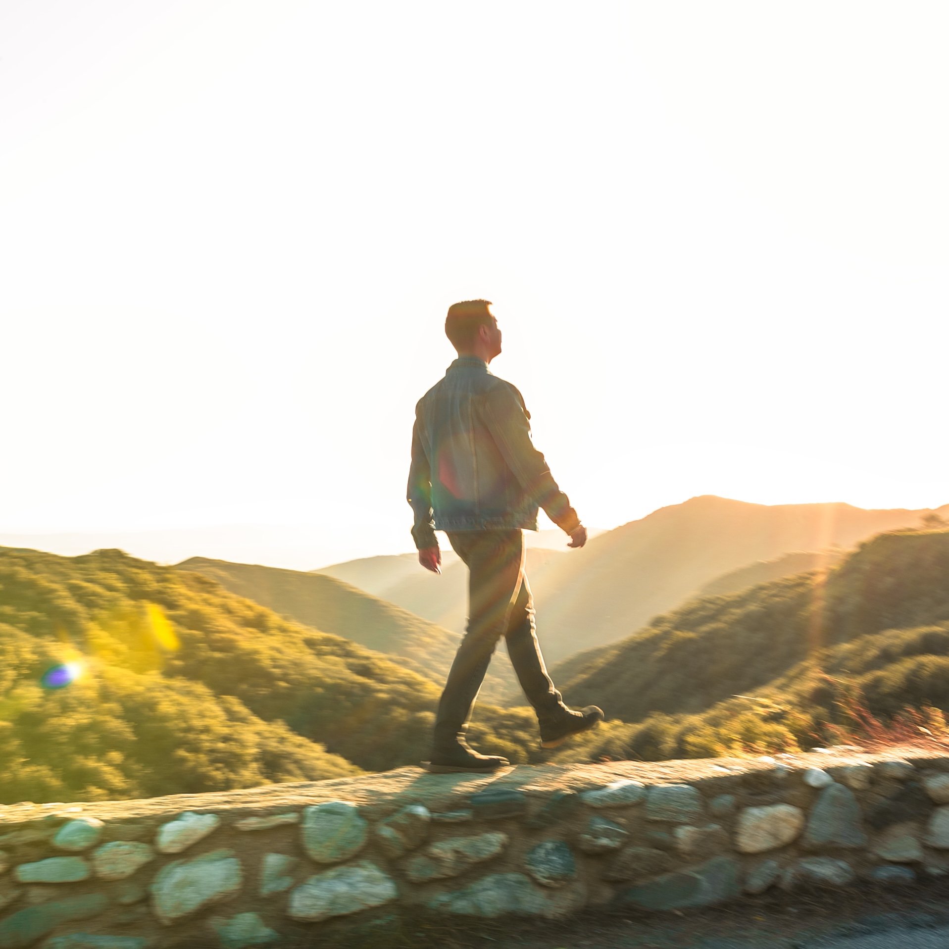 Person walking on a stone path in hills during sunset.