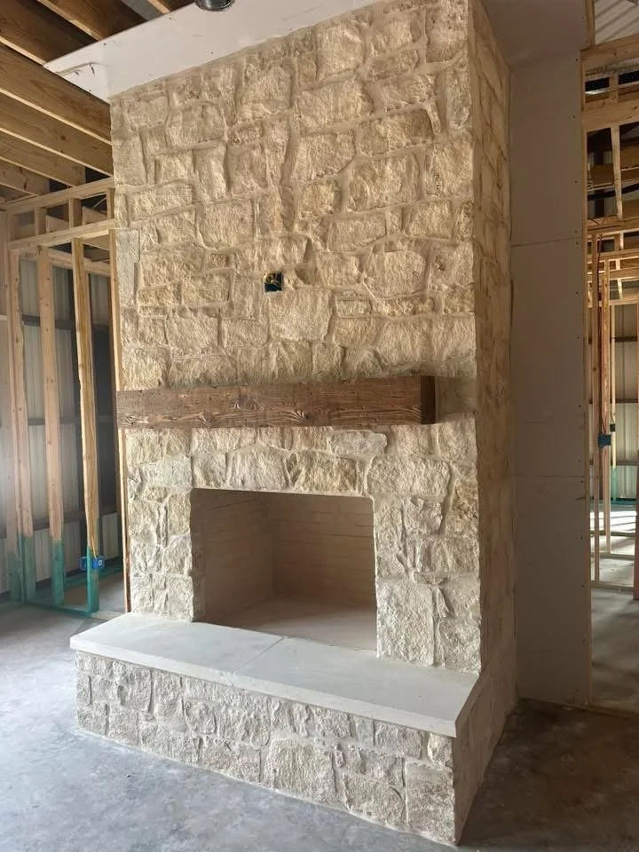 A stone fireplace under construction with unfinished wooden framing and a concrete and stone hearth inside a building still under construction.